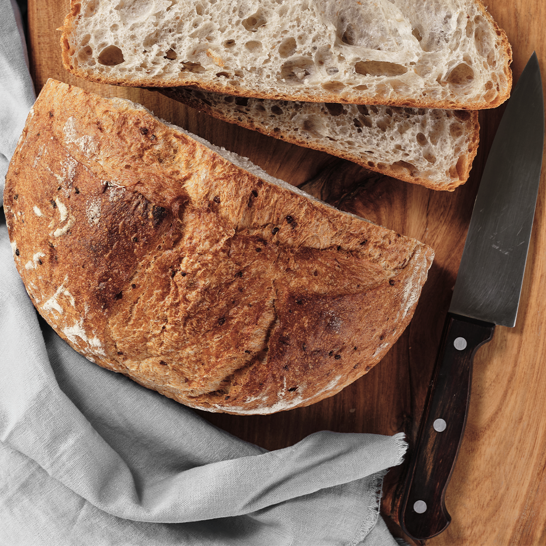 Slices of rustic, crusty bread on a wooden cutting board with a bread knife.