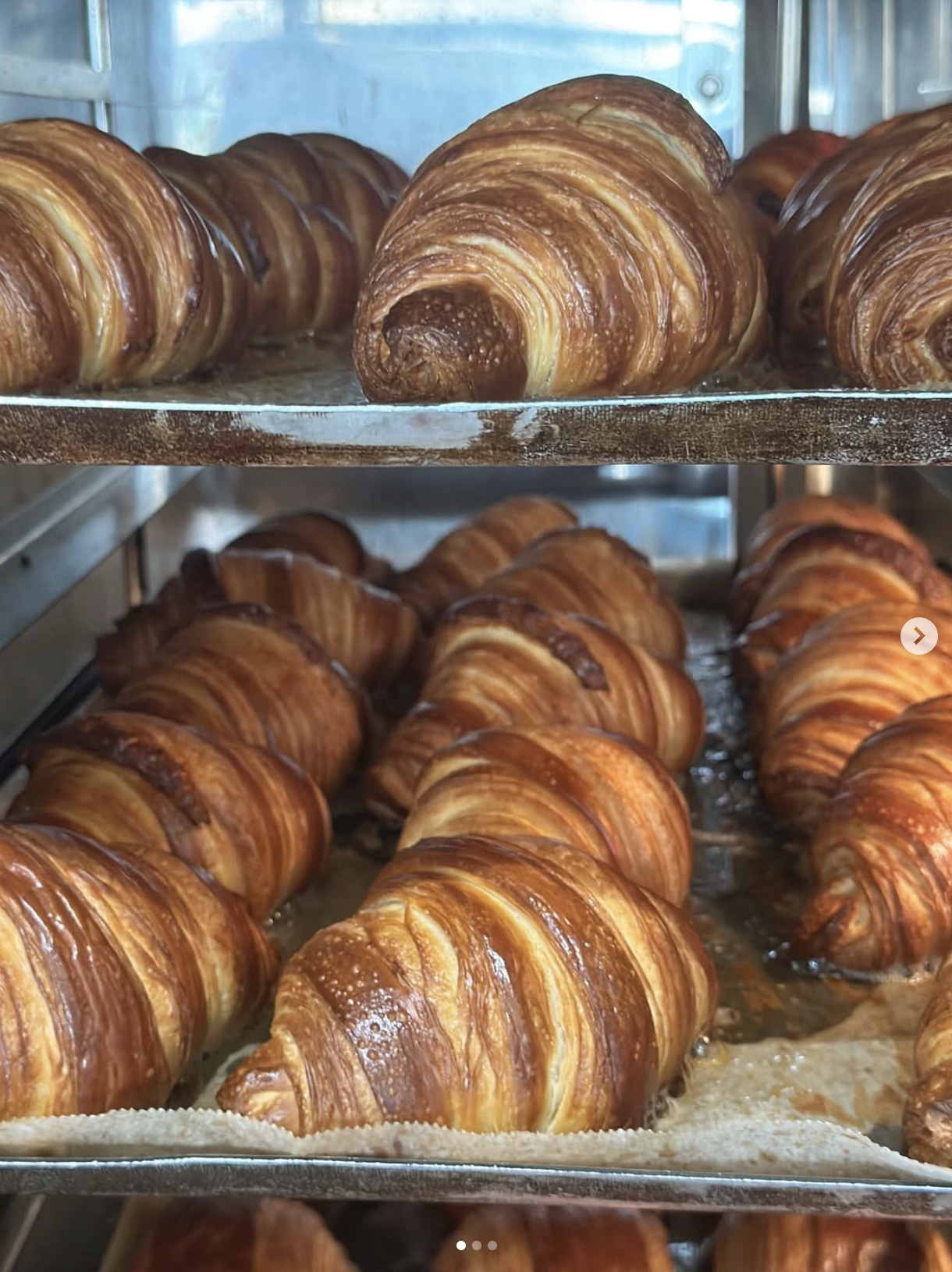 Close-up of freshly baked croissants on metal trays in a bakery display case.