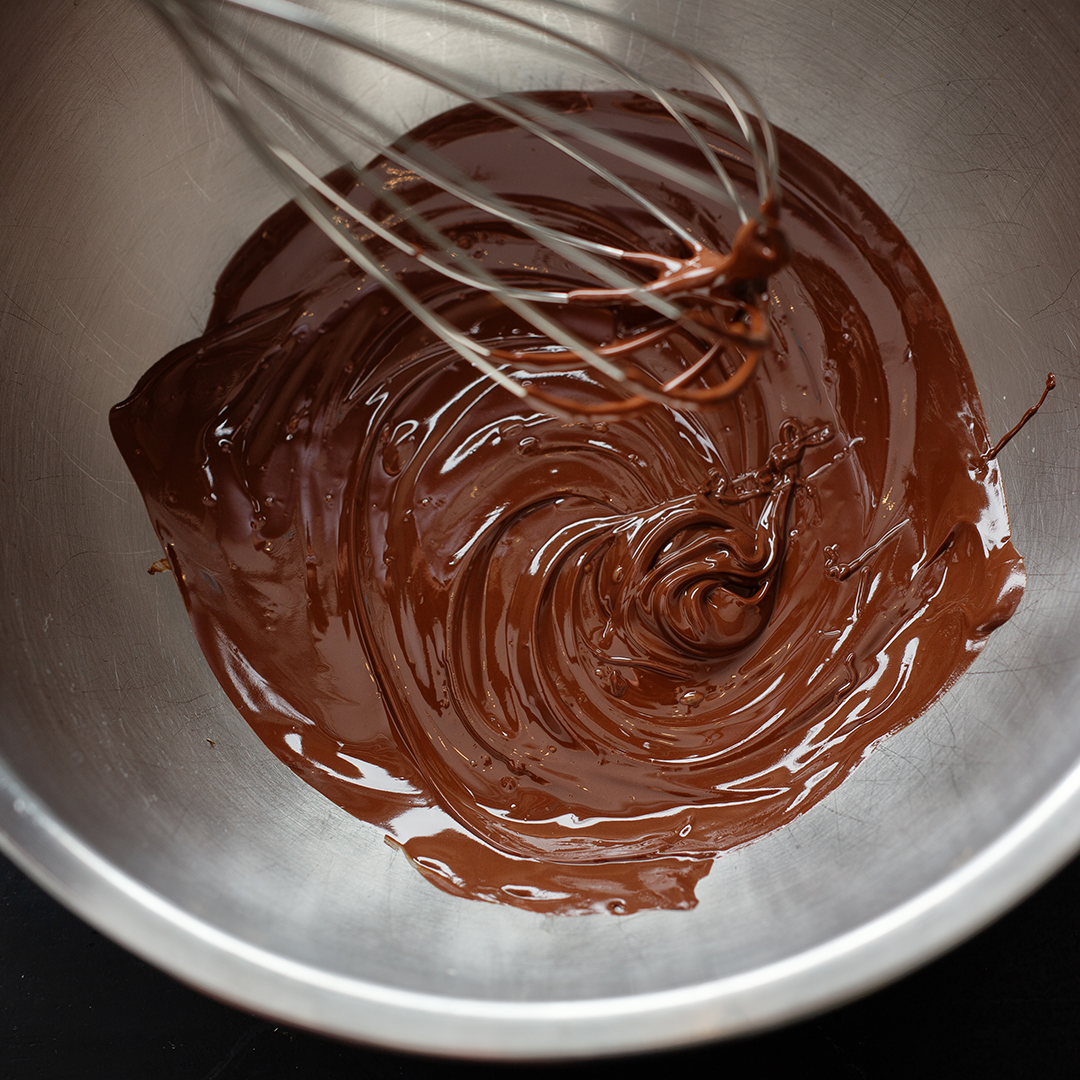 Melting chocolate in a metal mixing bowl with a whisk.