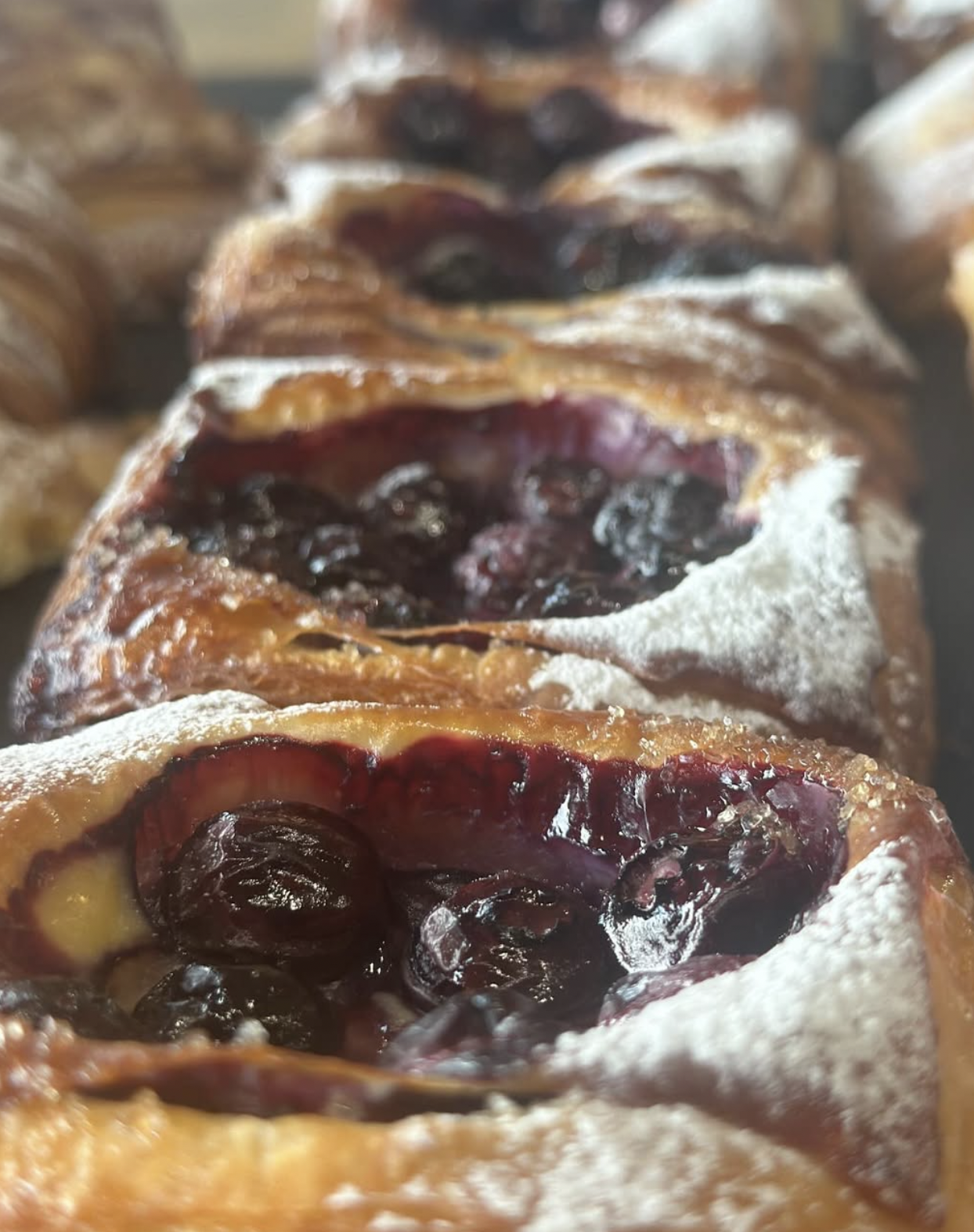 Close-up of cherry Danish pastries dusted with powdered sugar, arranged in a row.