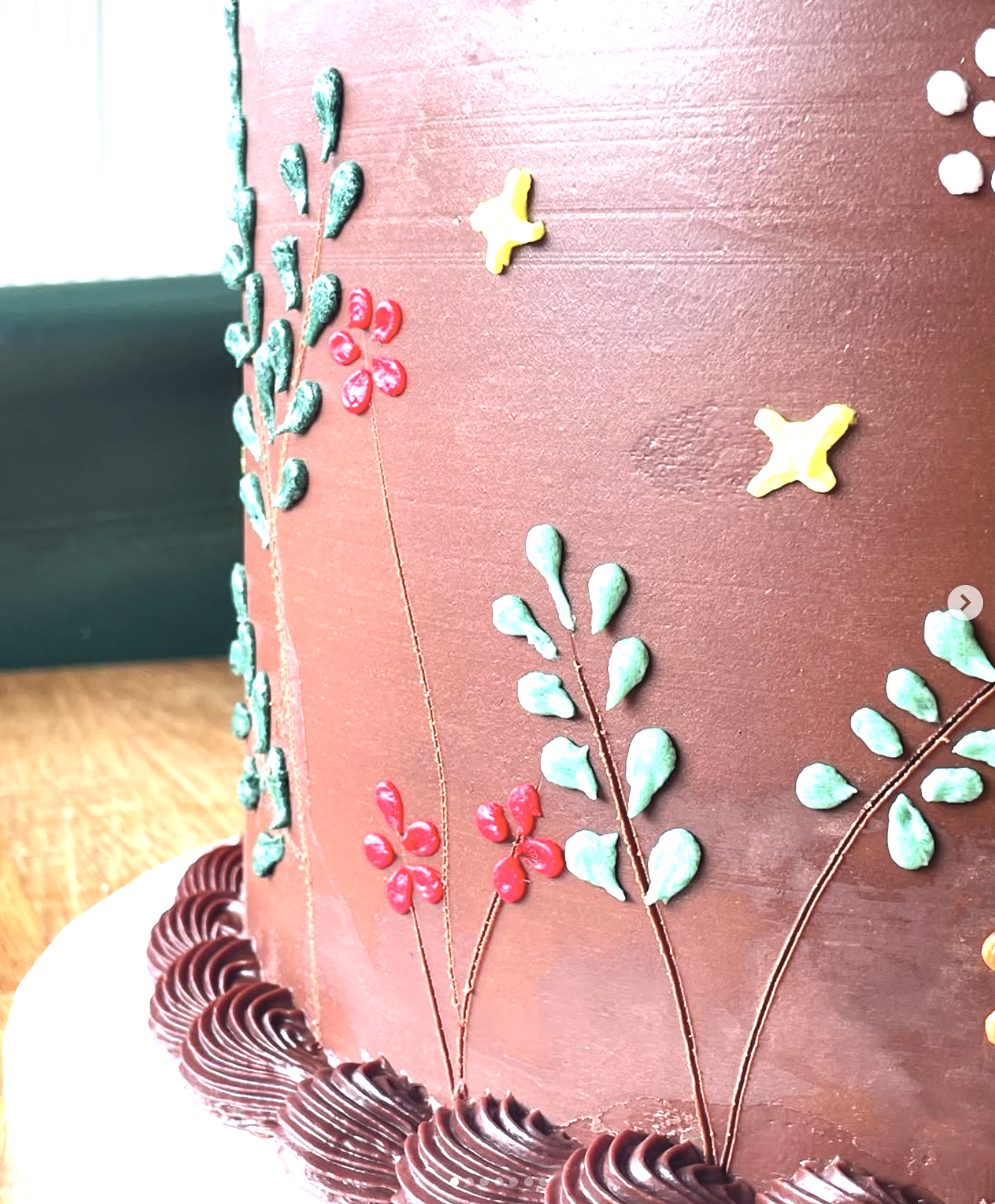 Close-up of a decorated chocolate cake with leaf and flower designs made of icing, and piped chocolate along the bottom edge.