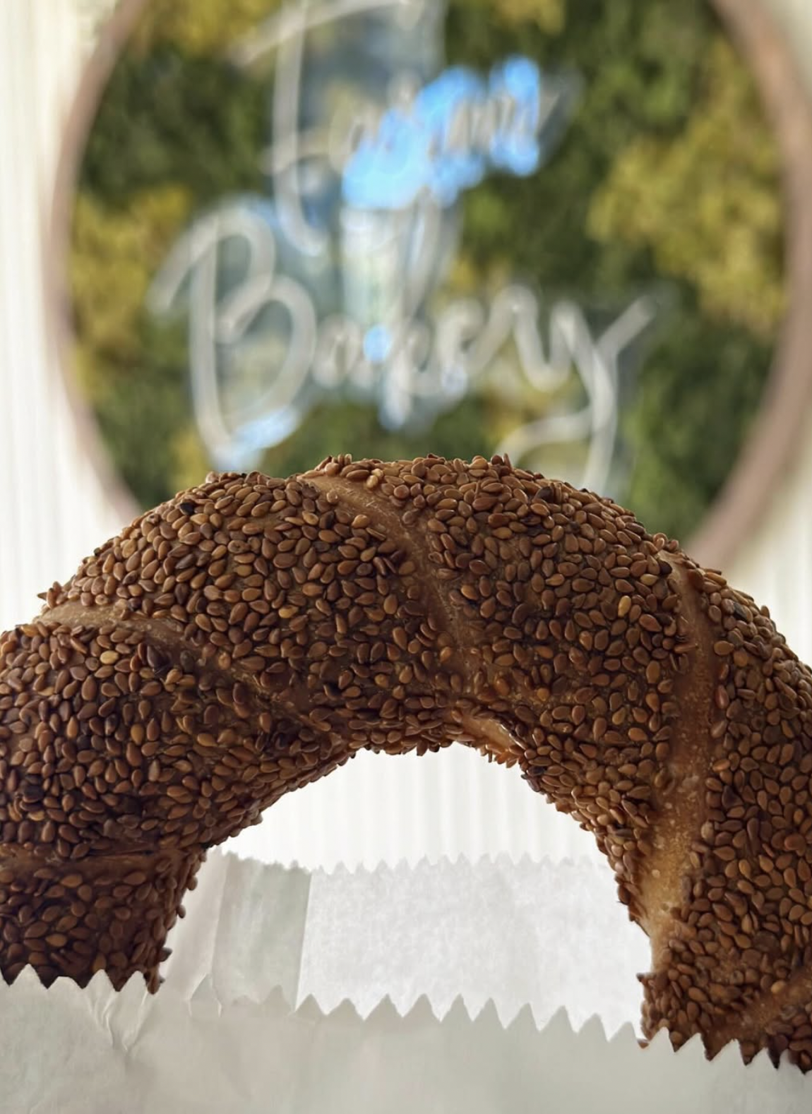 Close-up of a sesame seed-covered pastry with a window in the background showing the words 'Cafe Bakery' written in cursive.