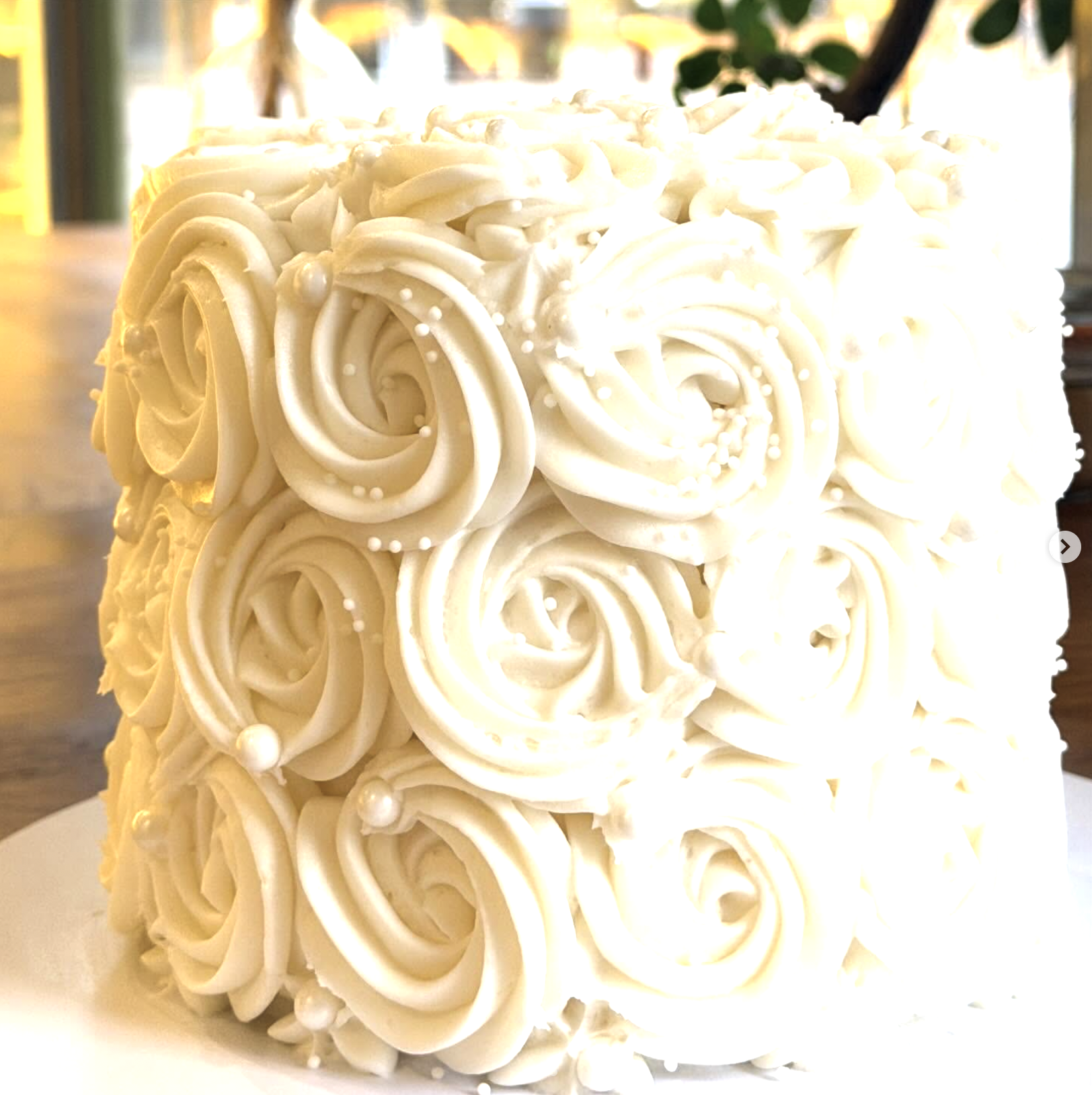 A white cake decorated with piped cream roses and small pearl-shaped sugar decorations.