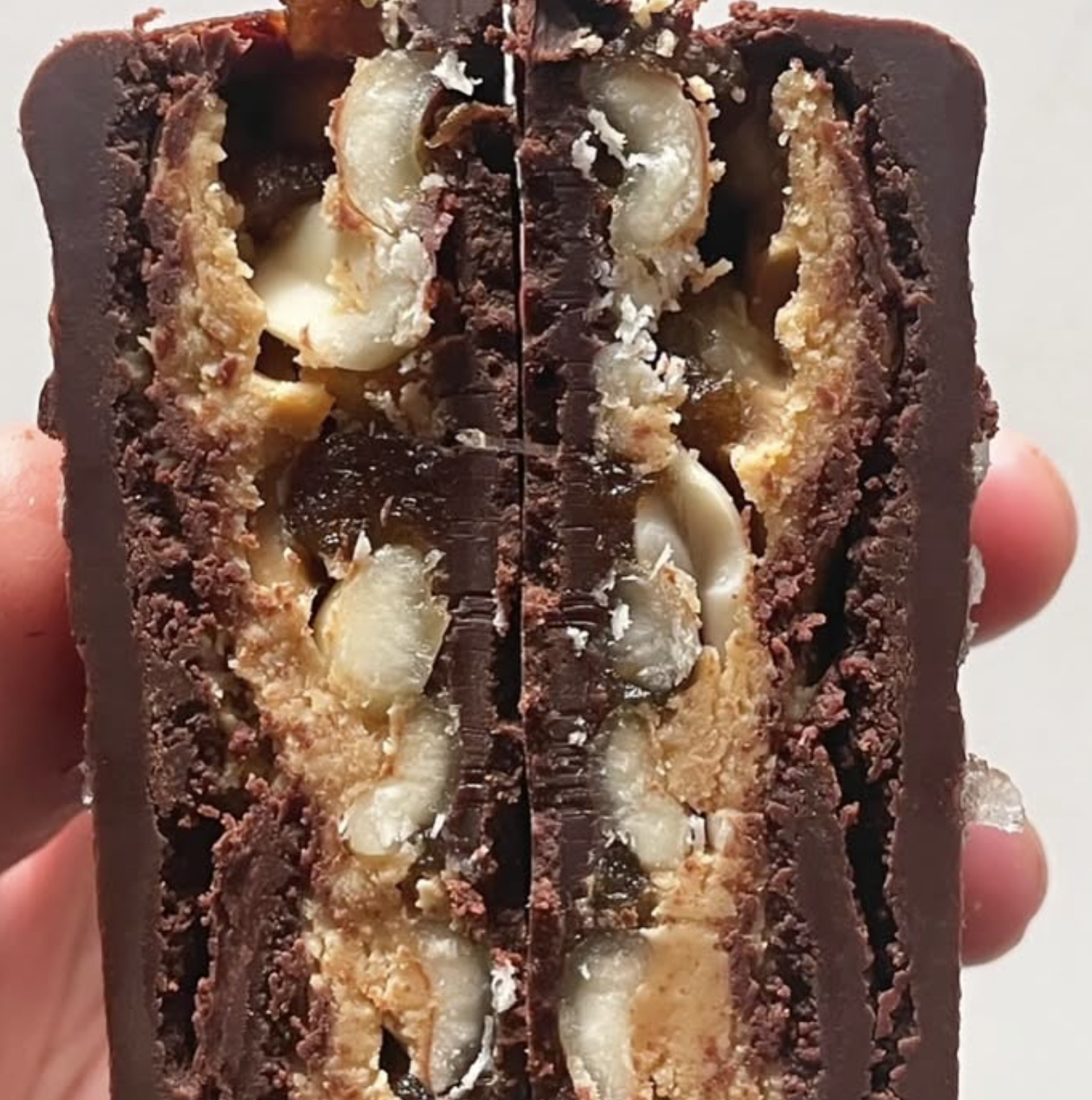 Cross-section of a layered chocolate and nut dessert bar with chocolate coating, crushed nuts, and caramel layers.