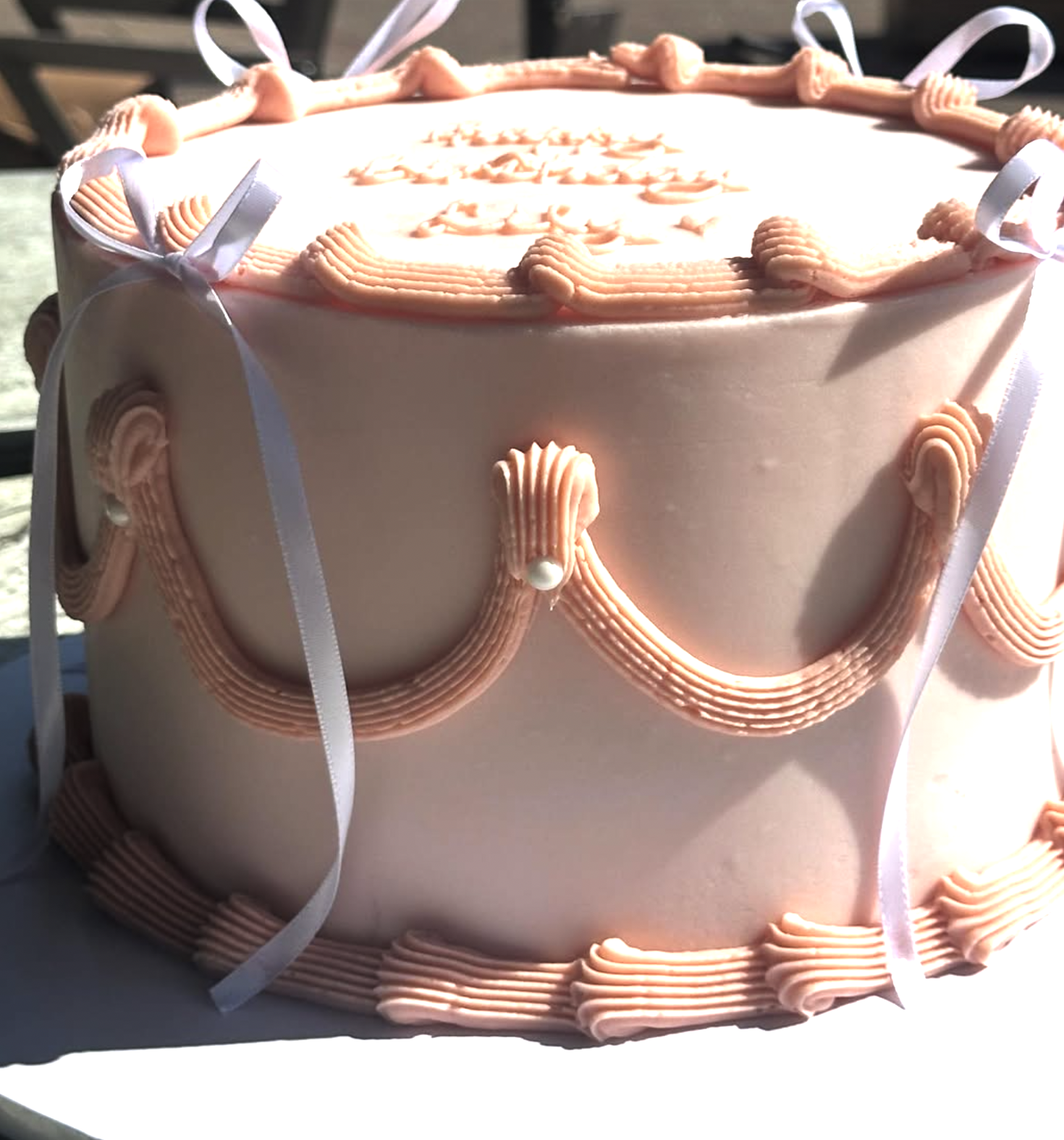 Pink decorative cake with piped borders and ribbons.