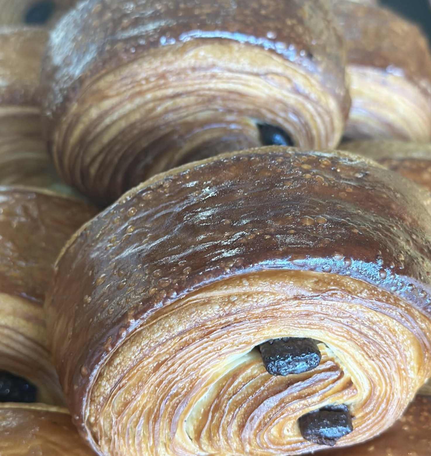 Close-up of several chocolate croissants with flaky, golden-brown layers and chocolate filling visible in some of the croissants.