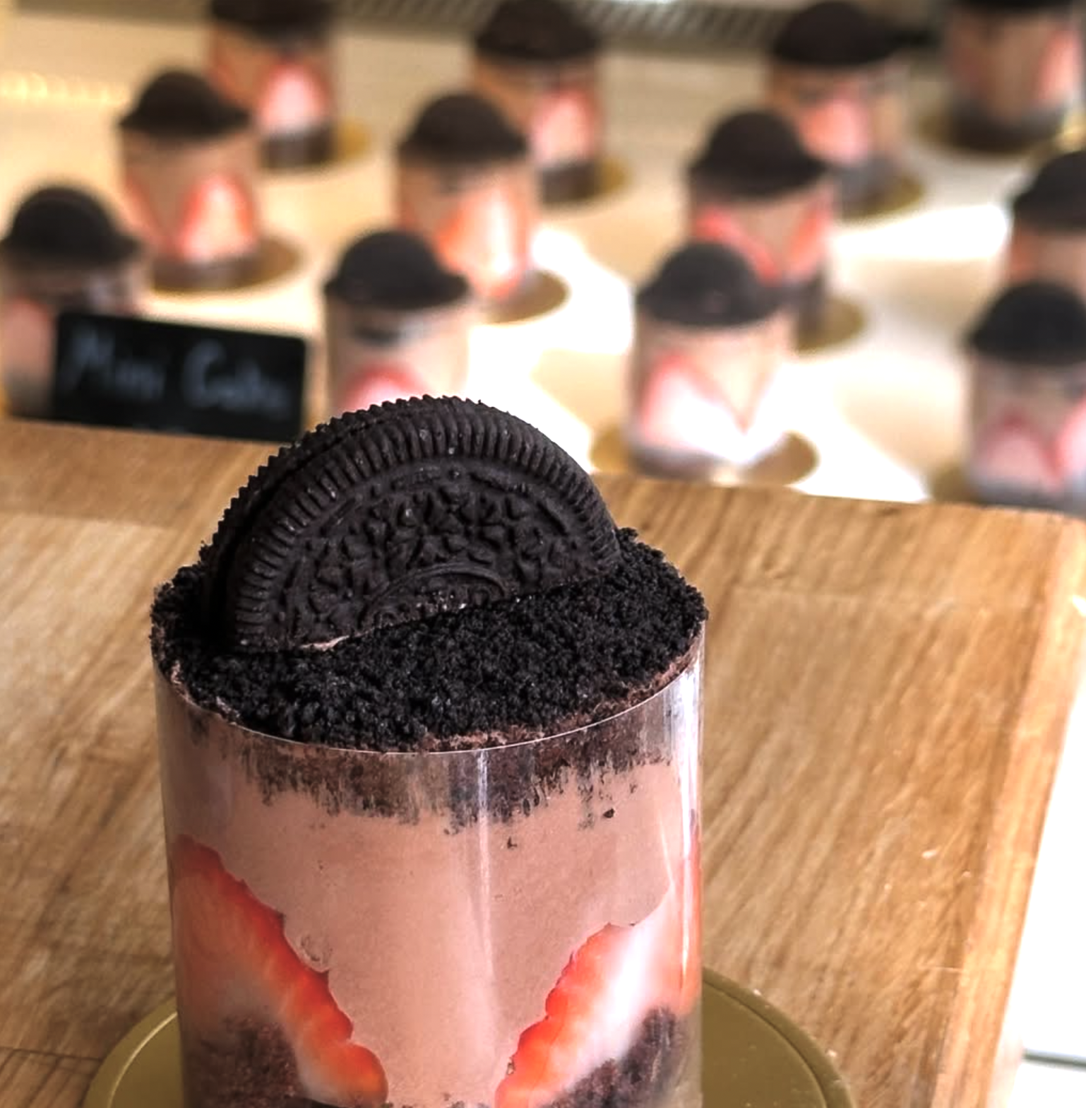 A layered oreo dessert with sliced strawberries, topped with crushed oreo cookies, and a whole oreo cookie on top, served on a golden plate on a wooden surface.