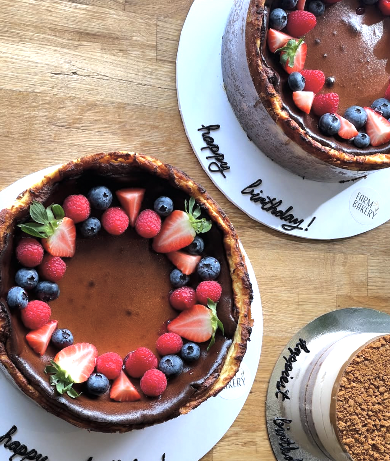 Two chocolate tarts decorated with fresh strawberries, blueberries, raspberries, and small green leaves on white plates with birthday messages.