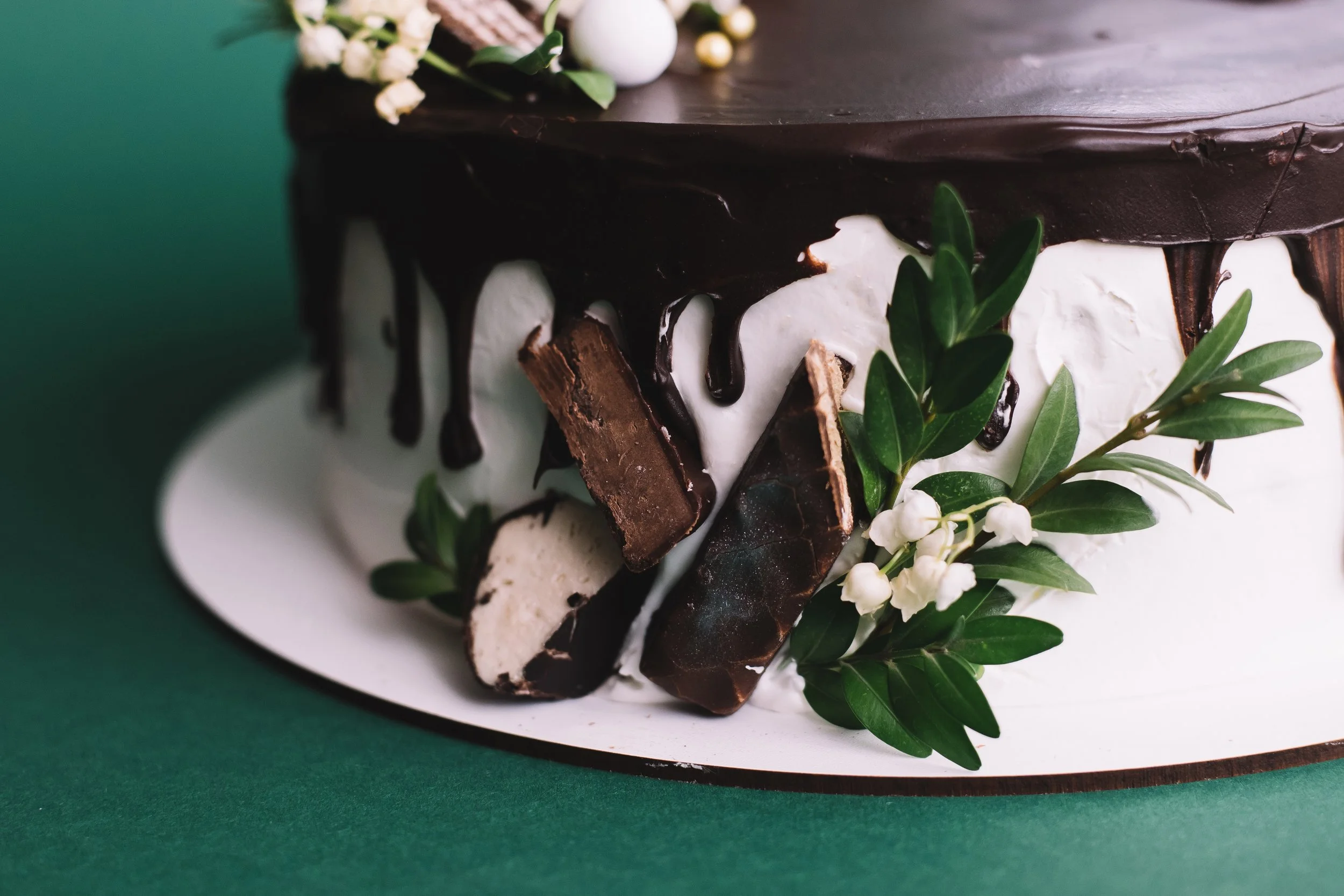Close-up of a chocolate cake decorated with chocolate bars, white flowers, and green leaves.