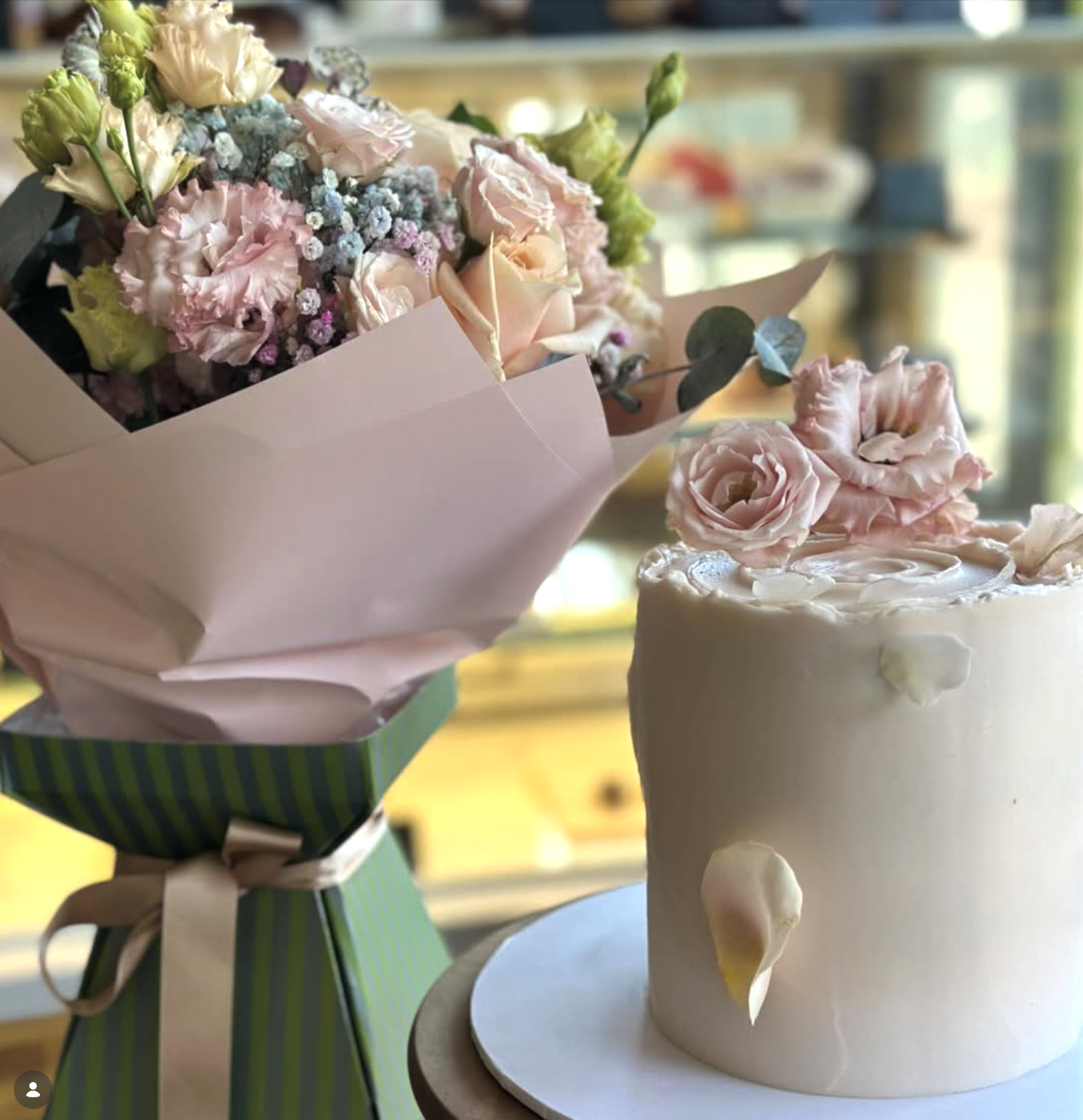 A pastel pink and green striped flower bouquet next to a white cake decorated with pink and white flowers.