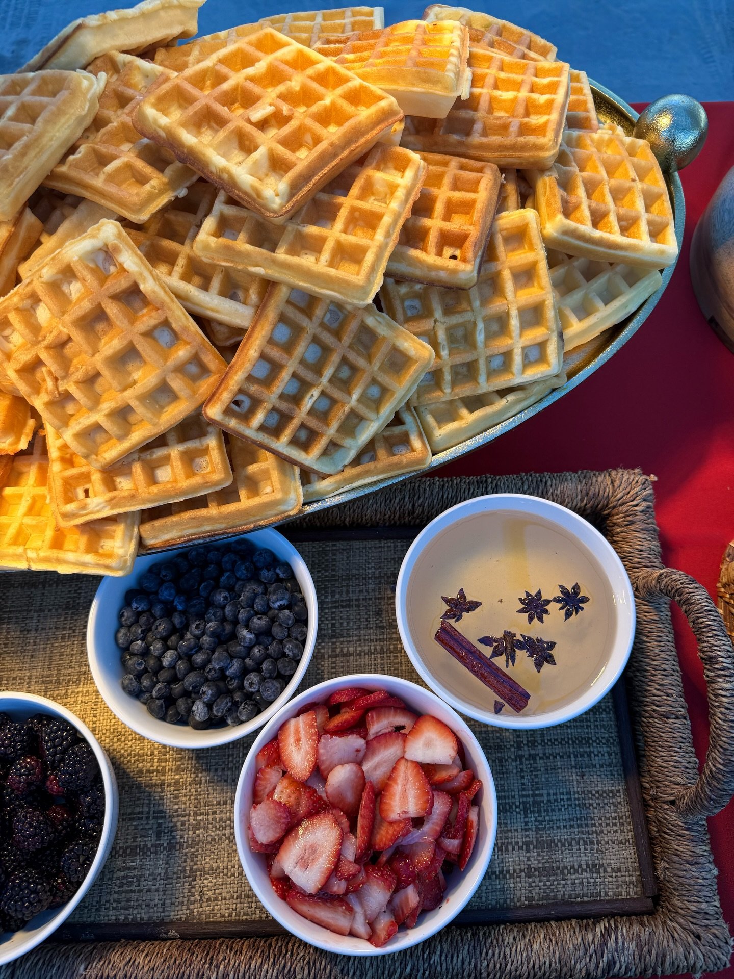 A tray of waffles with bowls of mixed berries and a cup of tea with herbs.