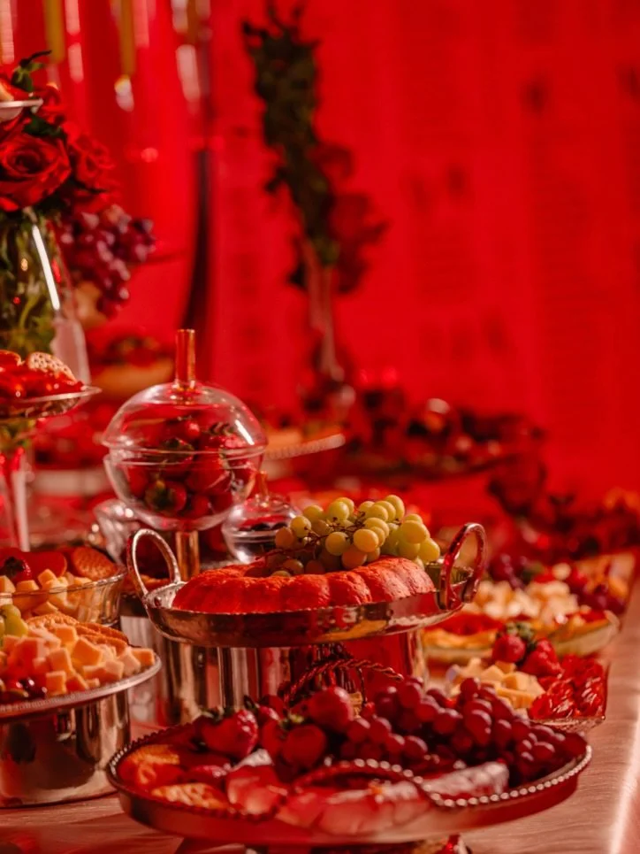 A festive table with various desserts, grapes, and strawberries, decorated with red ribbons and flowers.