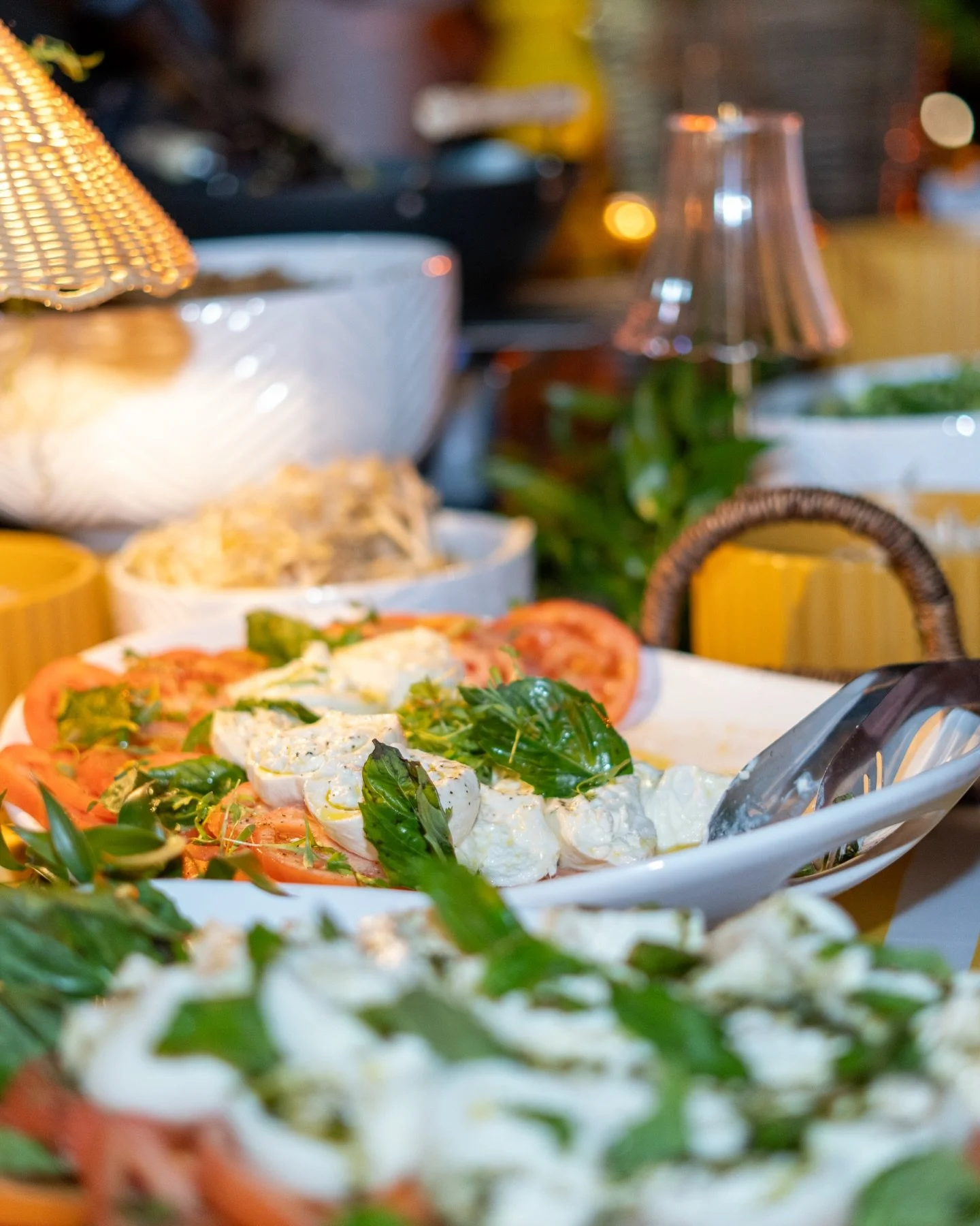 Fresh salad with tomatoes, mozzarella, basil, and greens on a white platter at a buffet table.