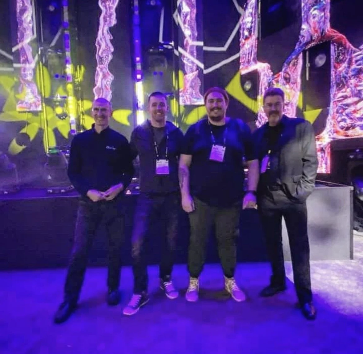 Four men standing together on a stage with colorful, digital abstract backgrounds.