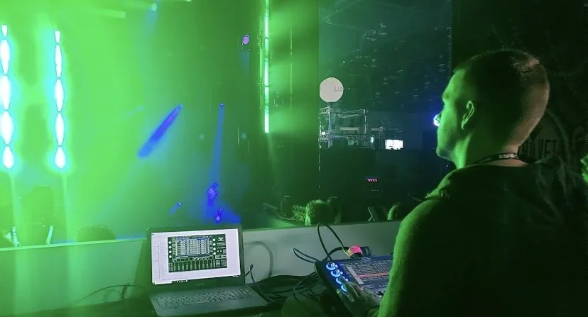 Lighting engineer working with sound and lighting equipment at a nightclub, with green and purple lights illuminating the scene.