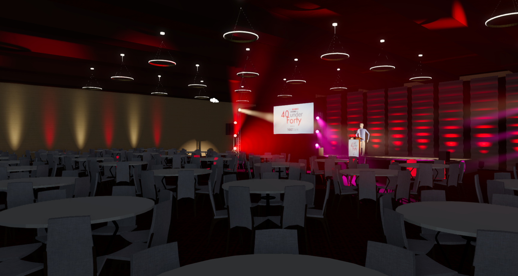Empty banquet hall with round tables and chairs, a stage with lighting and a large screen displaying '40 Under Forty,' and a man speaking at a podium.
