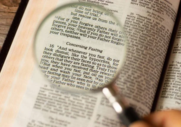 Open Bible with a magnifying glass focusing on a passage about fasting.