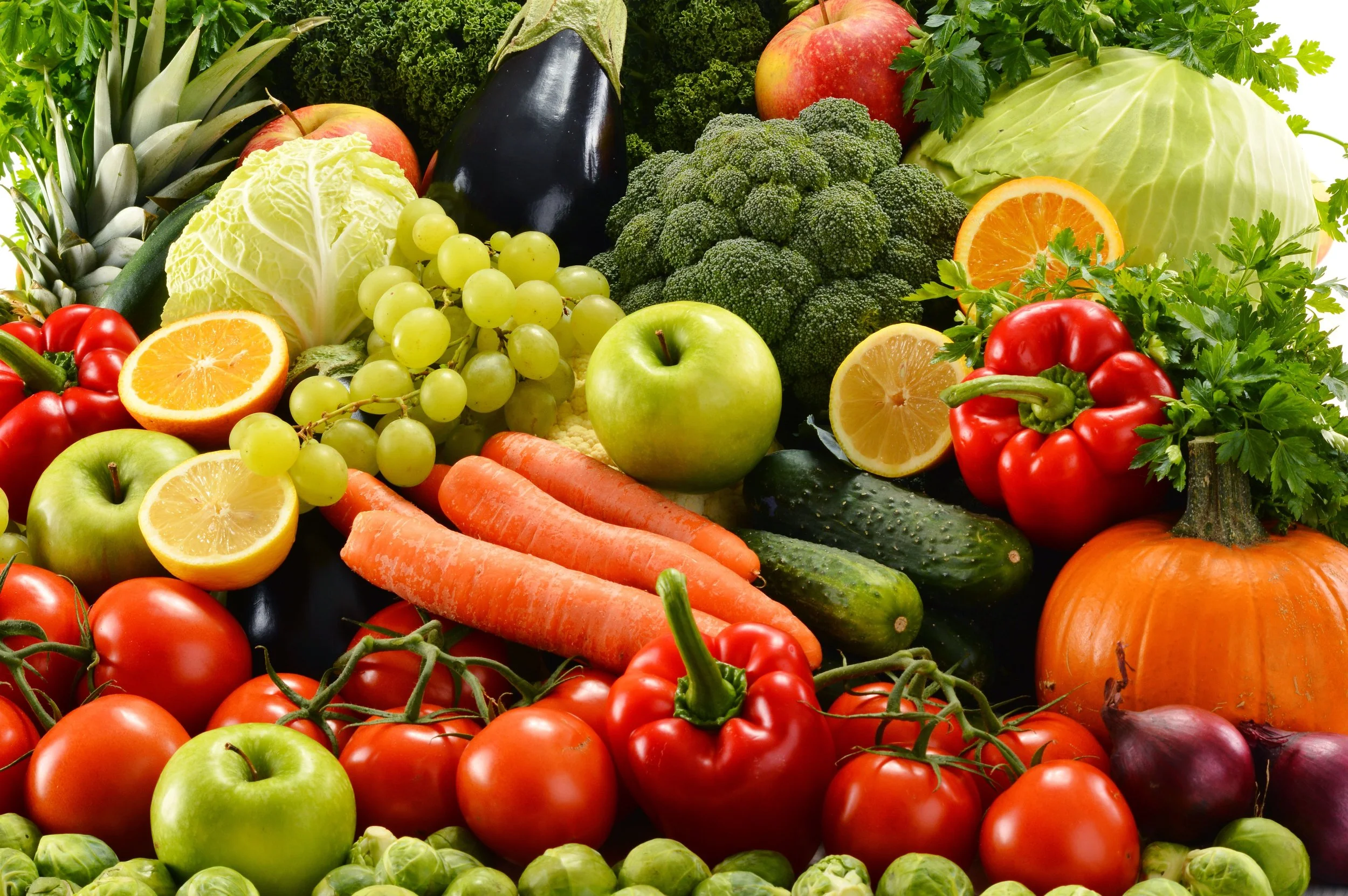 A colorful assortment of fresh fruits and vegetables including tomatoes, apples, oranges, carrots, cucumbers, broccoli, cabbage, red bell peppers, grapes, pineapple, eggplant, red onions, and parsley.