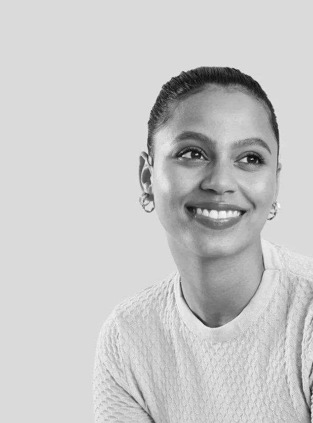Black and white portrait of a woman smiling, with her hair slicked back and wearing a textured top and earrings.