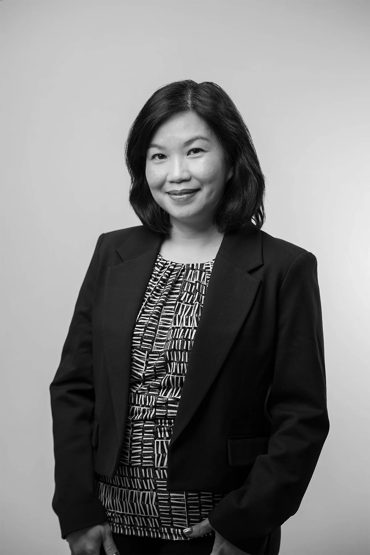 Black and white professional portrait of an Asian woman in a blazer, smiling, against a plain background.