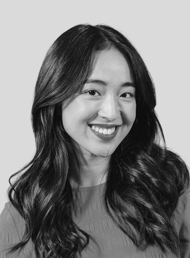 Black and white portrait of a woman with long, wavy hair, smiling and wearing a top.