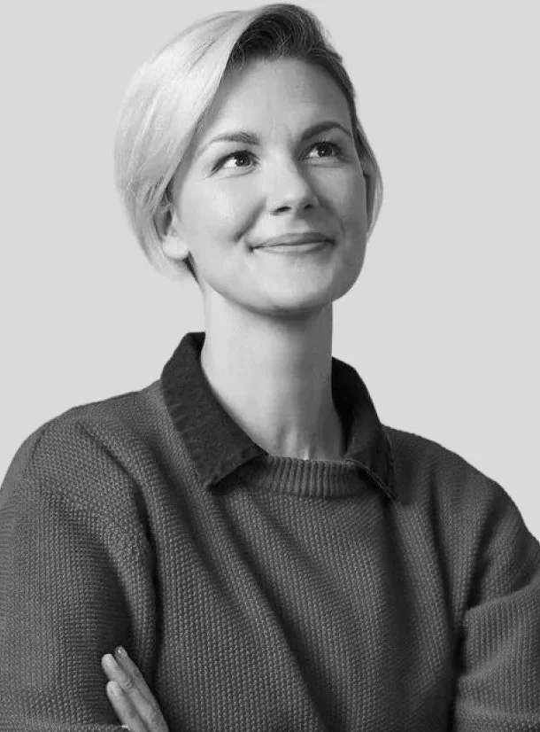 Black and white photo of a woman with short blonde hair, smiling and looking slightly upward, wearing a textured sweater.