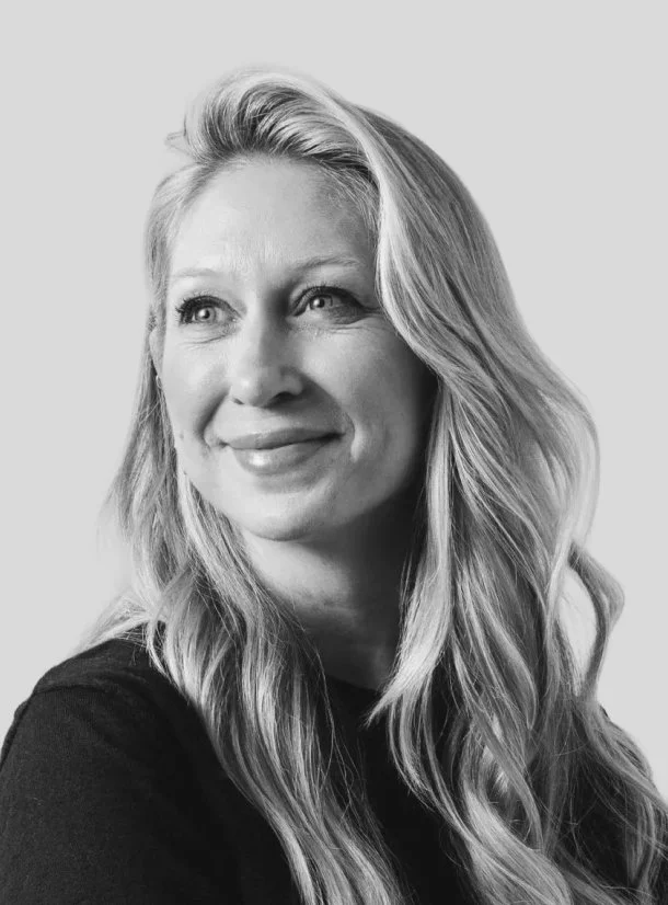 Black and white portrait of a woman with wavy blonde hair, smiling slightly and looking to the side.