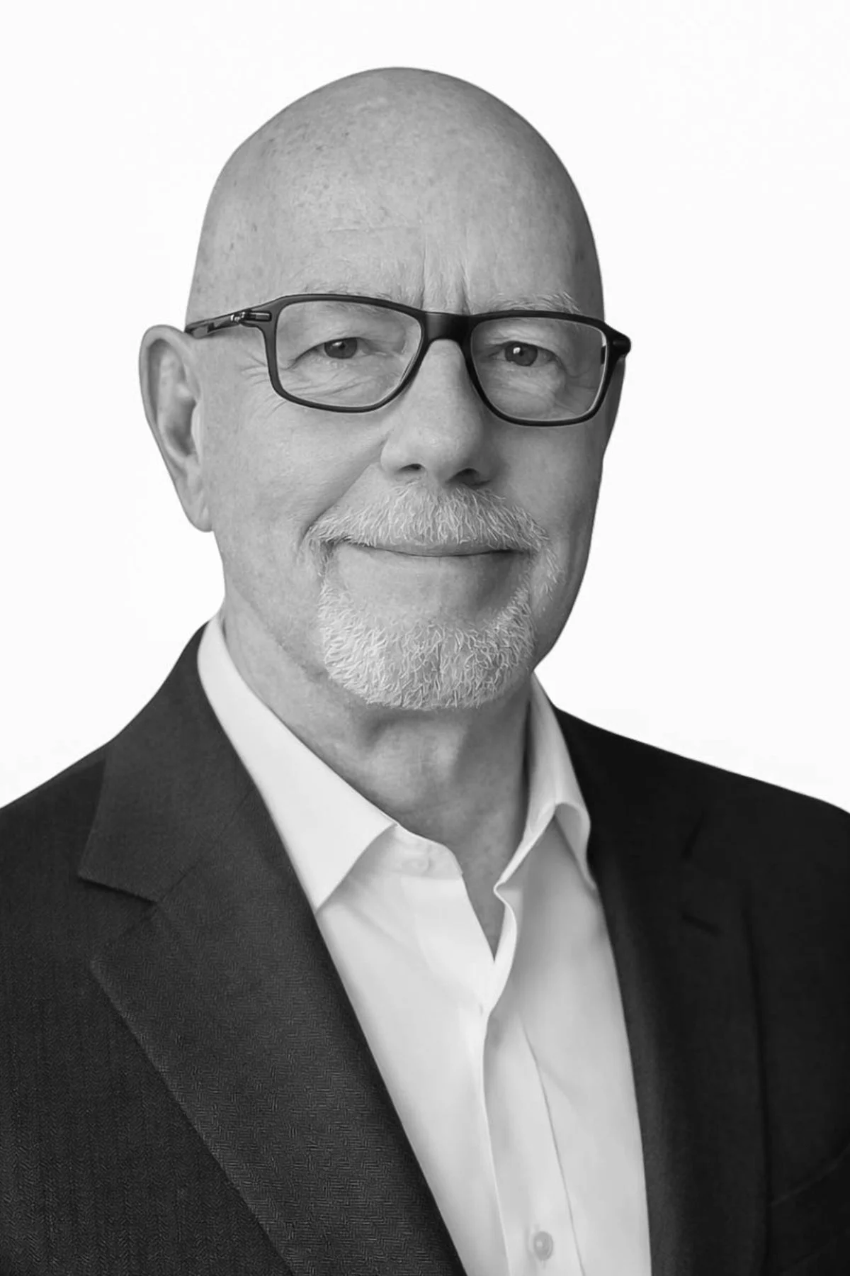 Black and white portrait of a senior man with glasses, a beard, and a bald head, wearing a suit and white shirt.