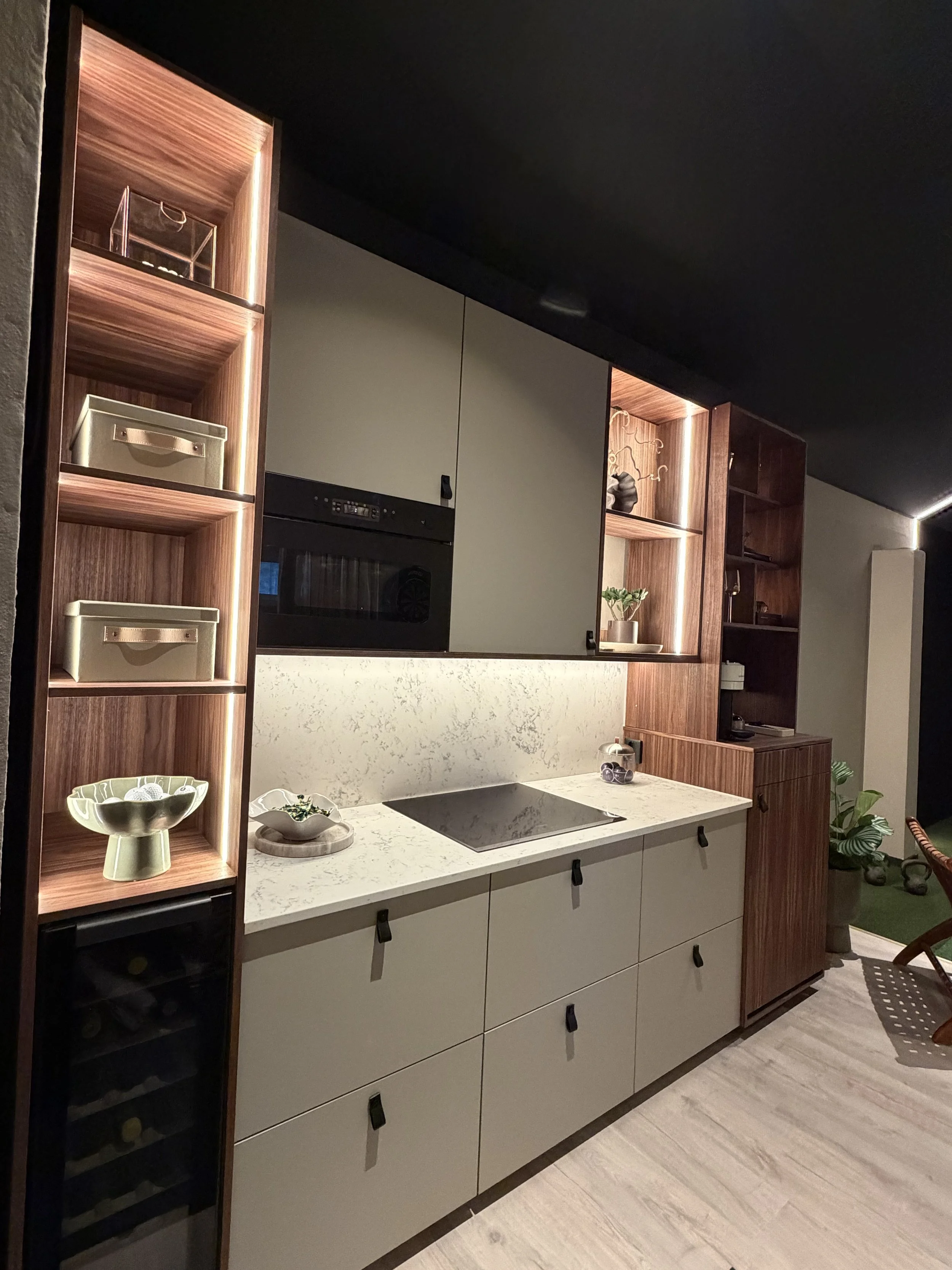 Kök med ljusgrå skåp, trähyllor och väggar, svart spishäll, inbyggd ugn, dekorativa föremål och växter