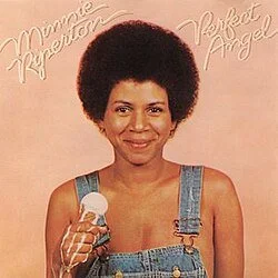 Woman with an afro hairstyle holding an ice cream cone, smiling, wearing denim overalls, album cover titled 'Minnie Riperton: Perfect Angel' in pink cursive