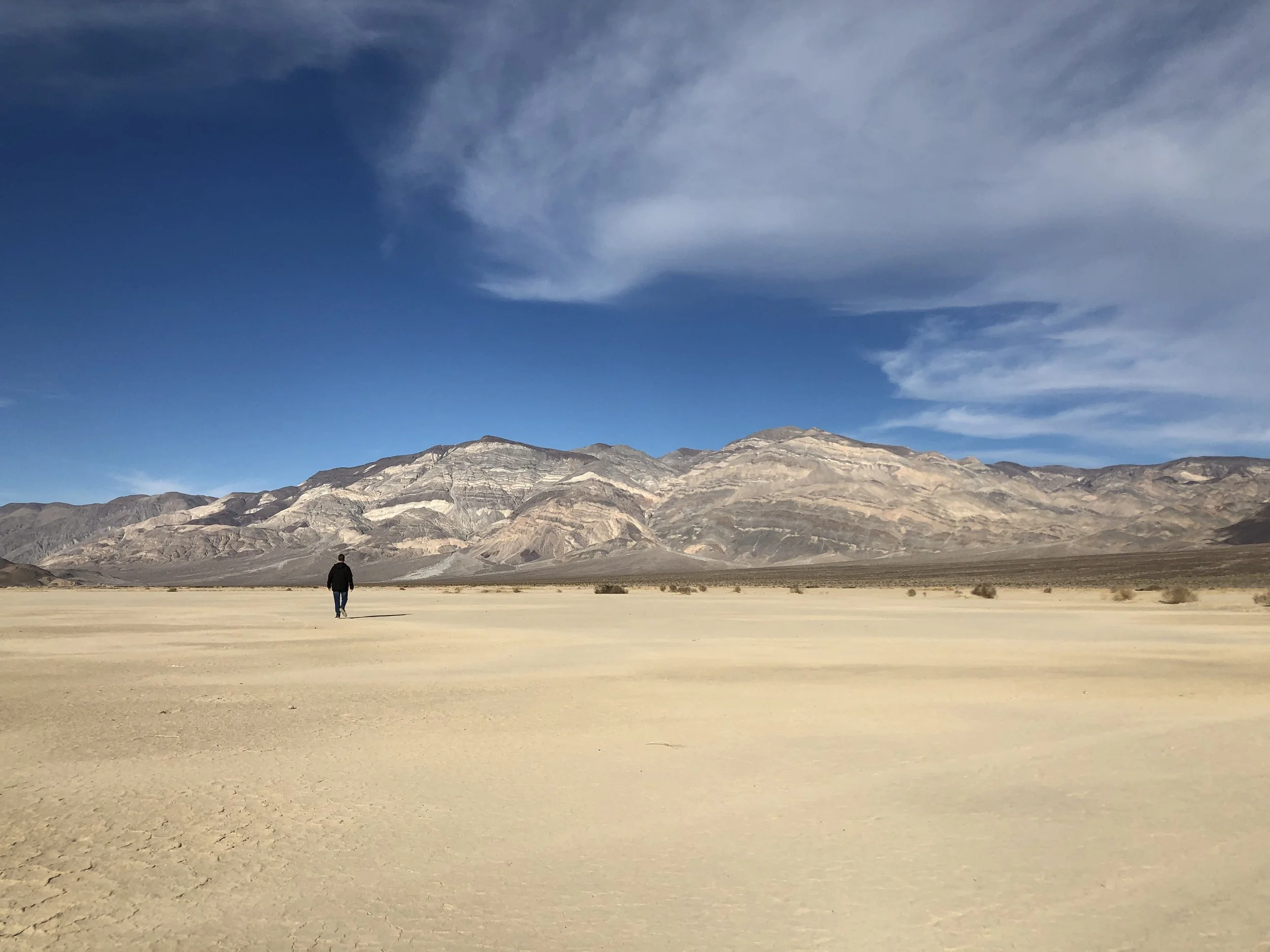 A person walking in a desert landscape with mountains and a cloudy sky in the background.