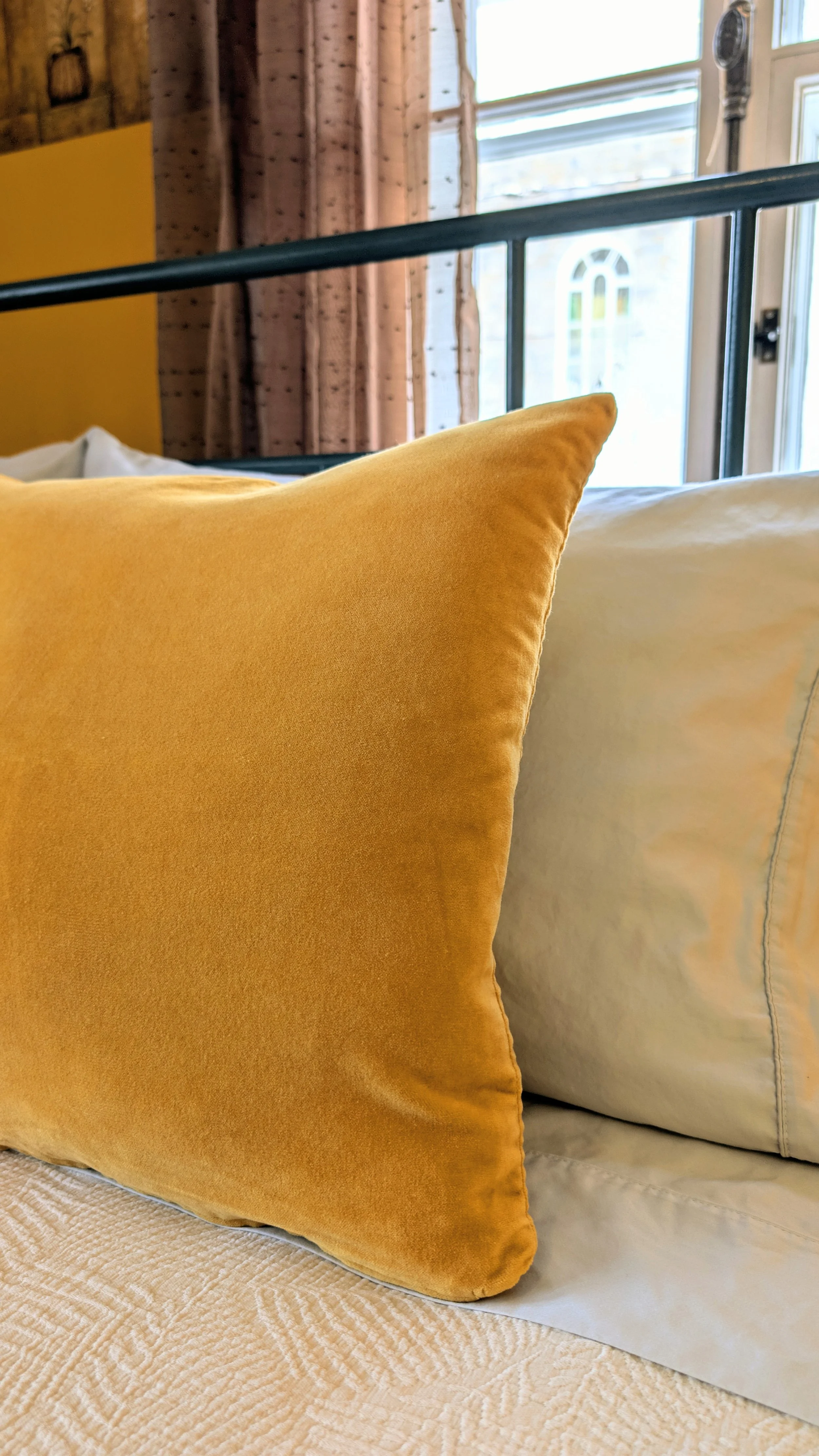 Vue rapprochée des textiles de la Chambre La Miellée, avec la vue des vitraux de l'église de Saint-Damien en arrière-plan