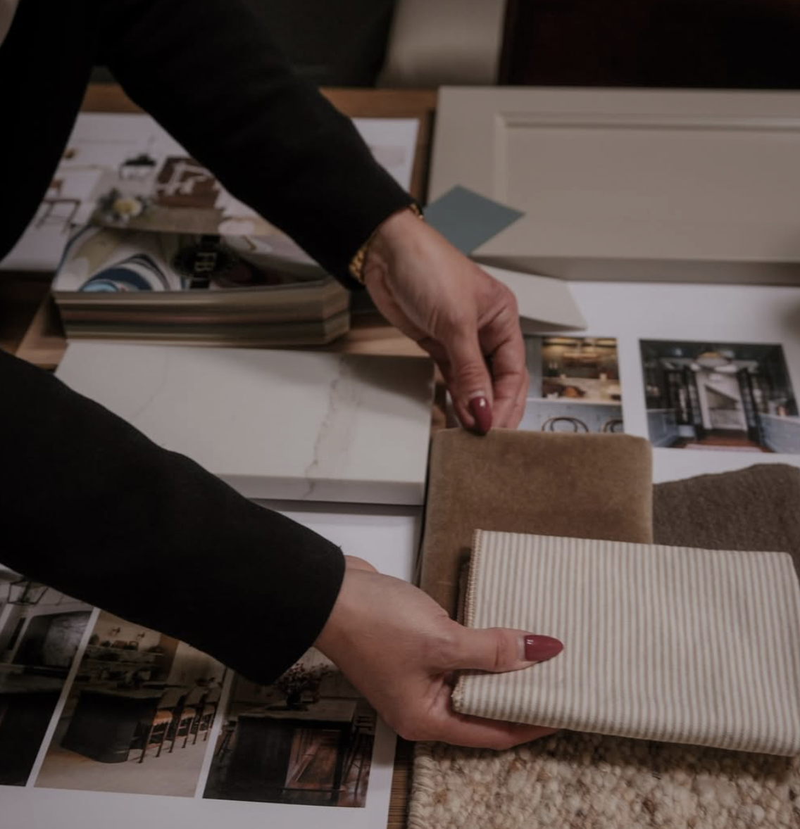 Two hands organizing fabric samples and design plans on a table for interior decorating.