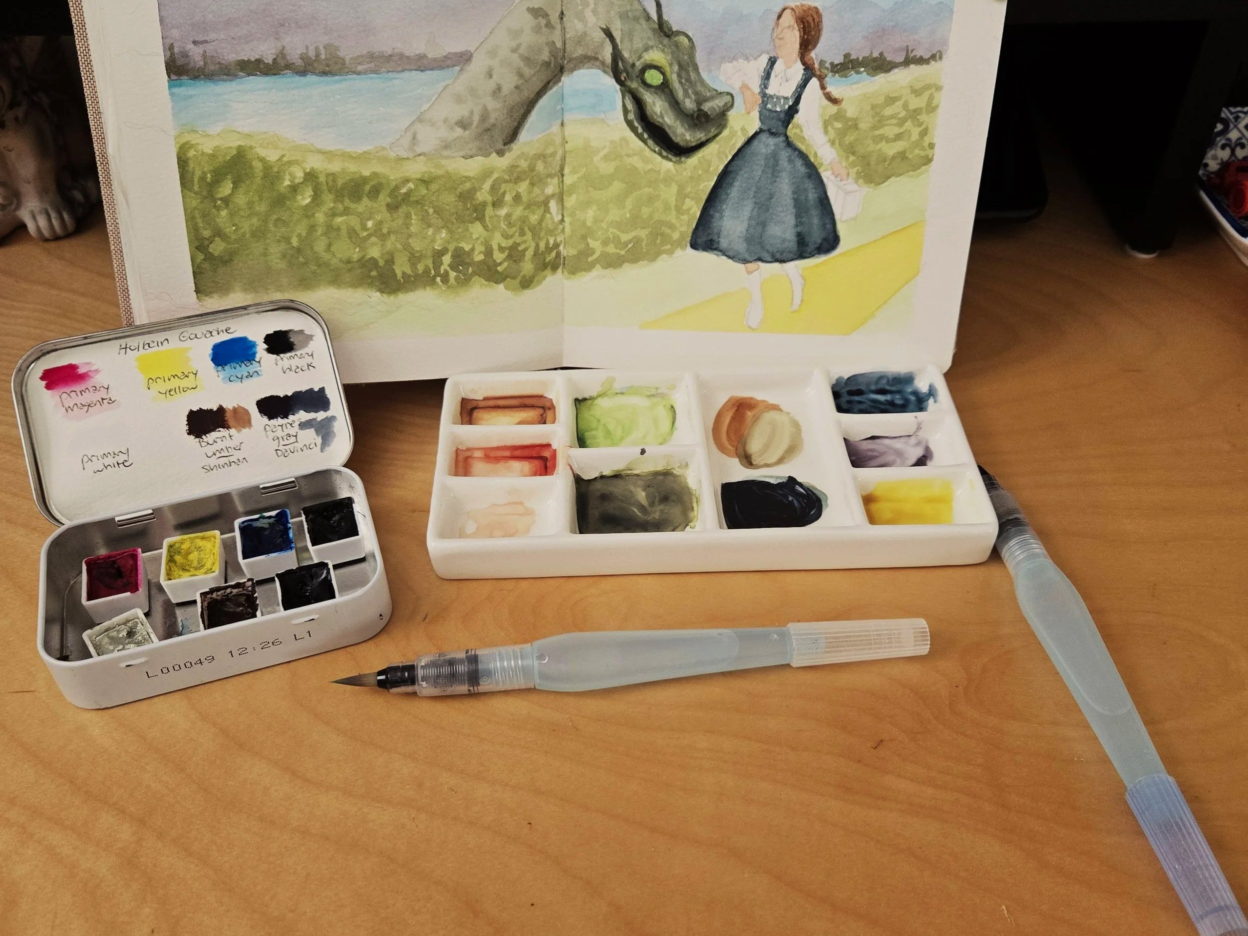Goauche painting in a sketchbook with paint pallette and water brushes on table