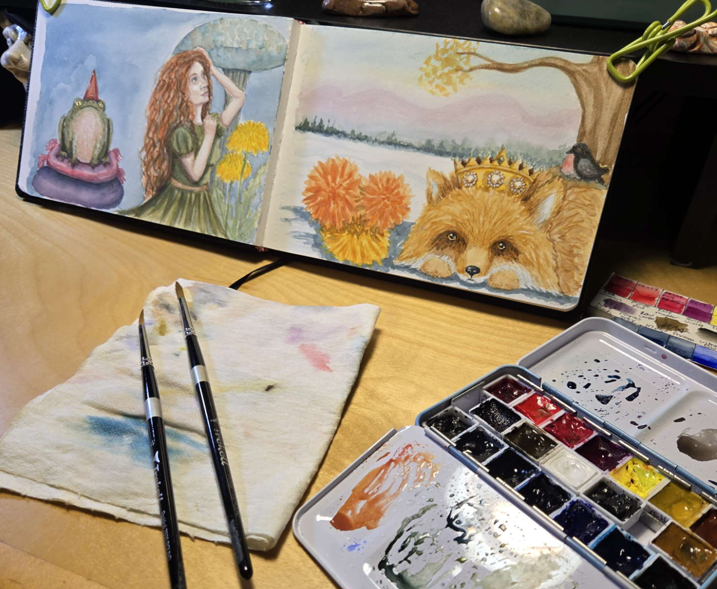watercolor sketchbook on a table with brushes and watercolor pallette