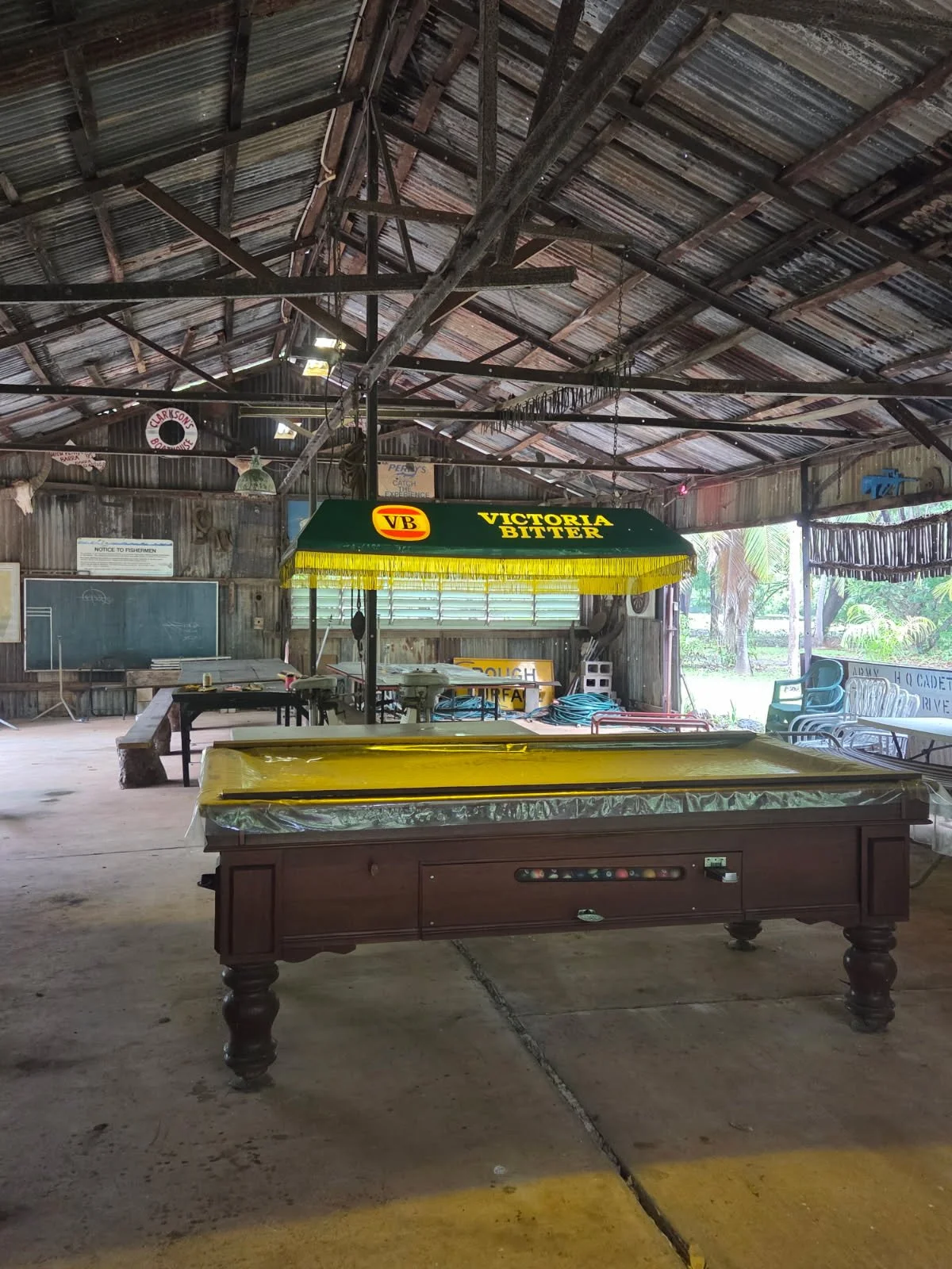 An empty rustic indoor space with a pool table in the foreground and a gaming table with a yellow umbrella in the background.
