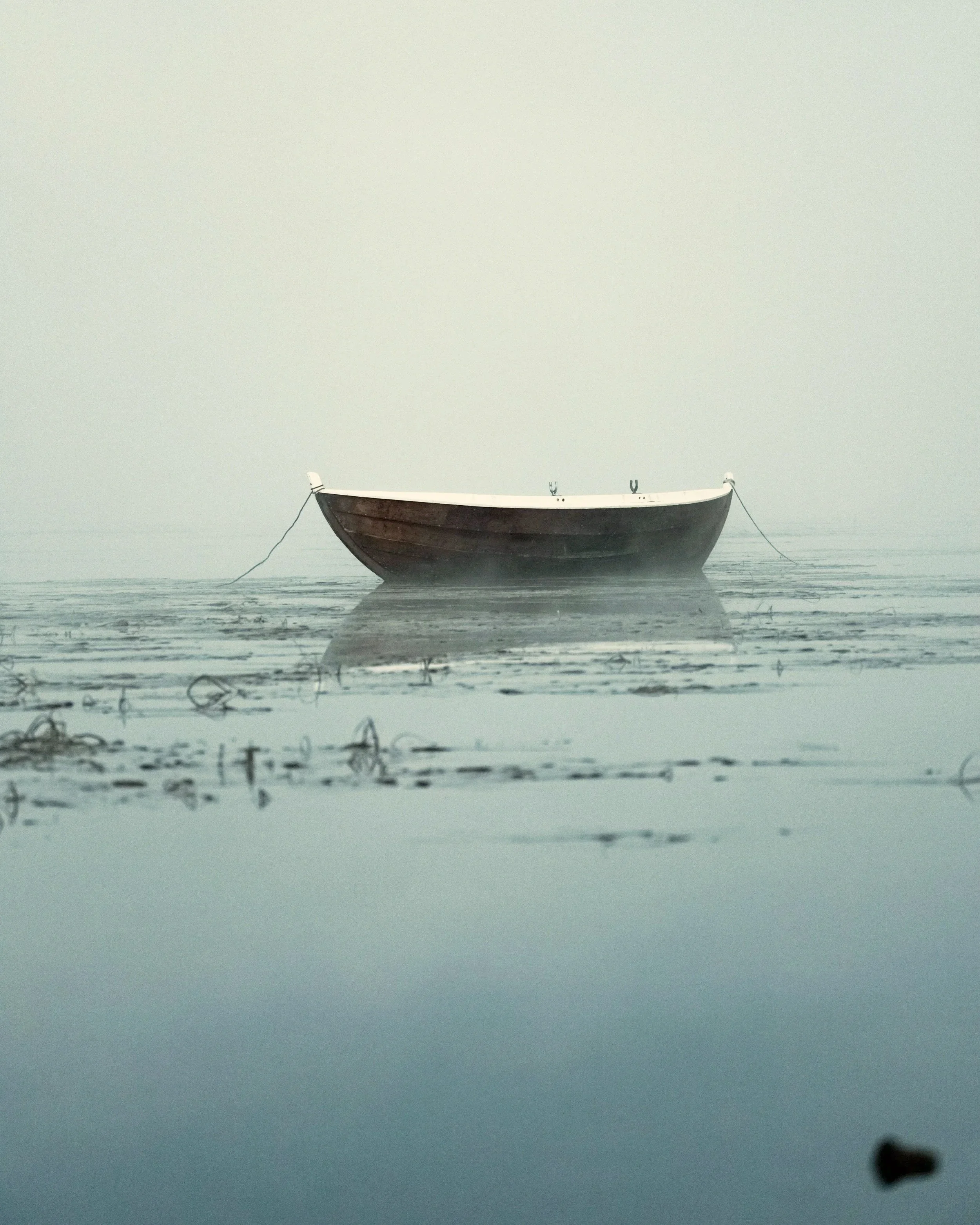 A small boat floating on calm, foggy water.