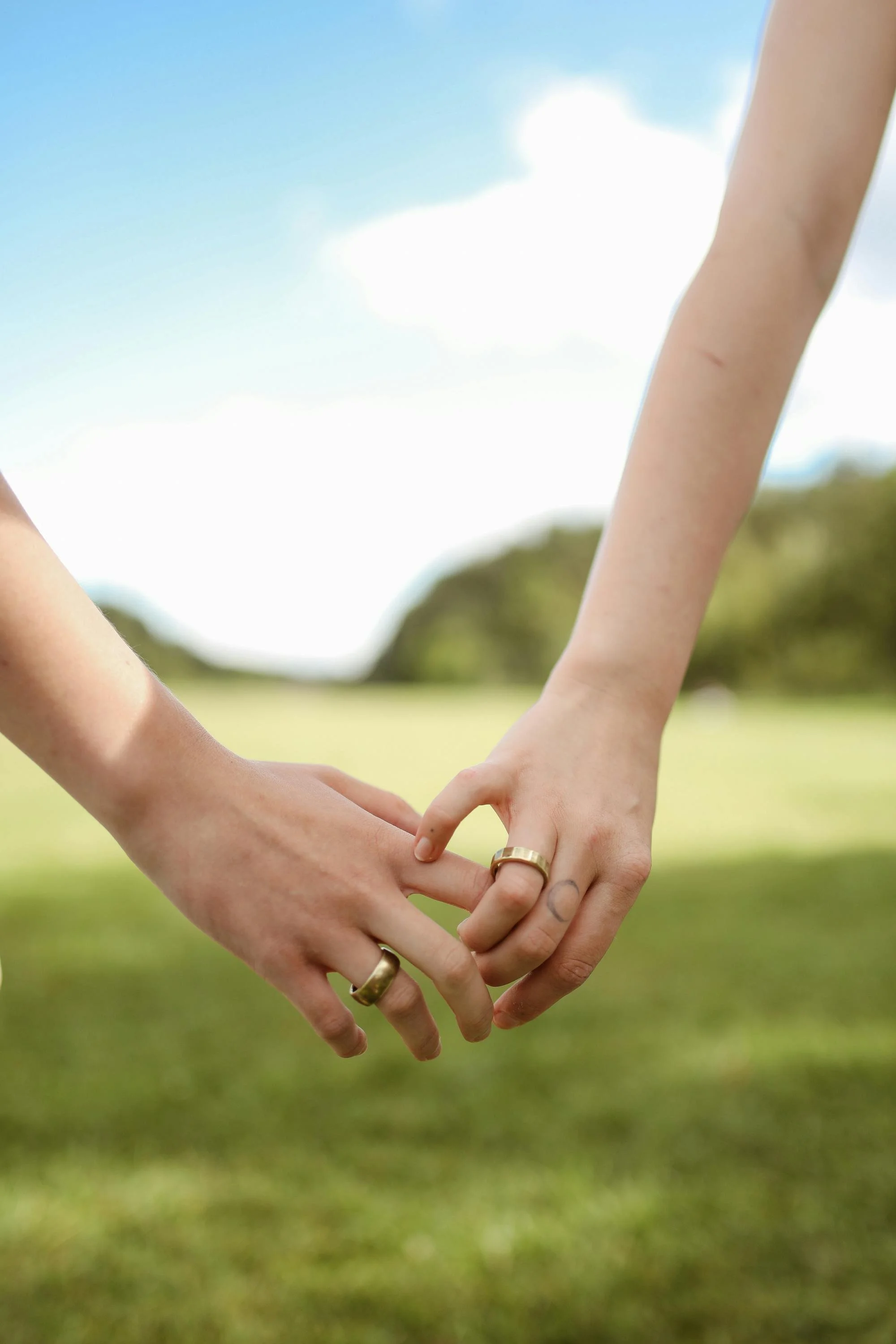 Two people, wearing wedding bands, touching hands.