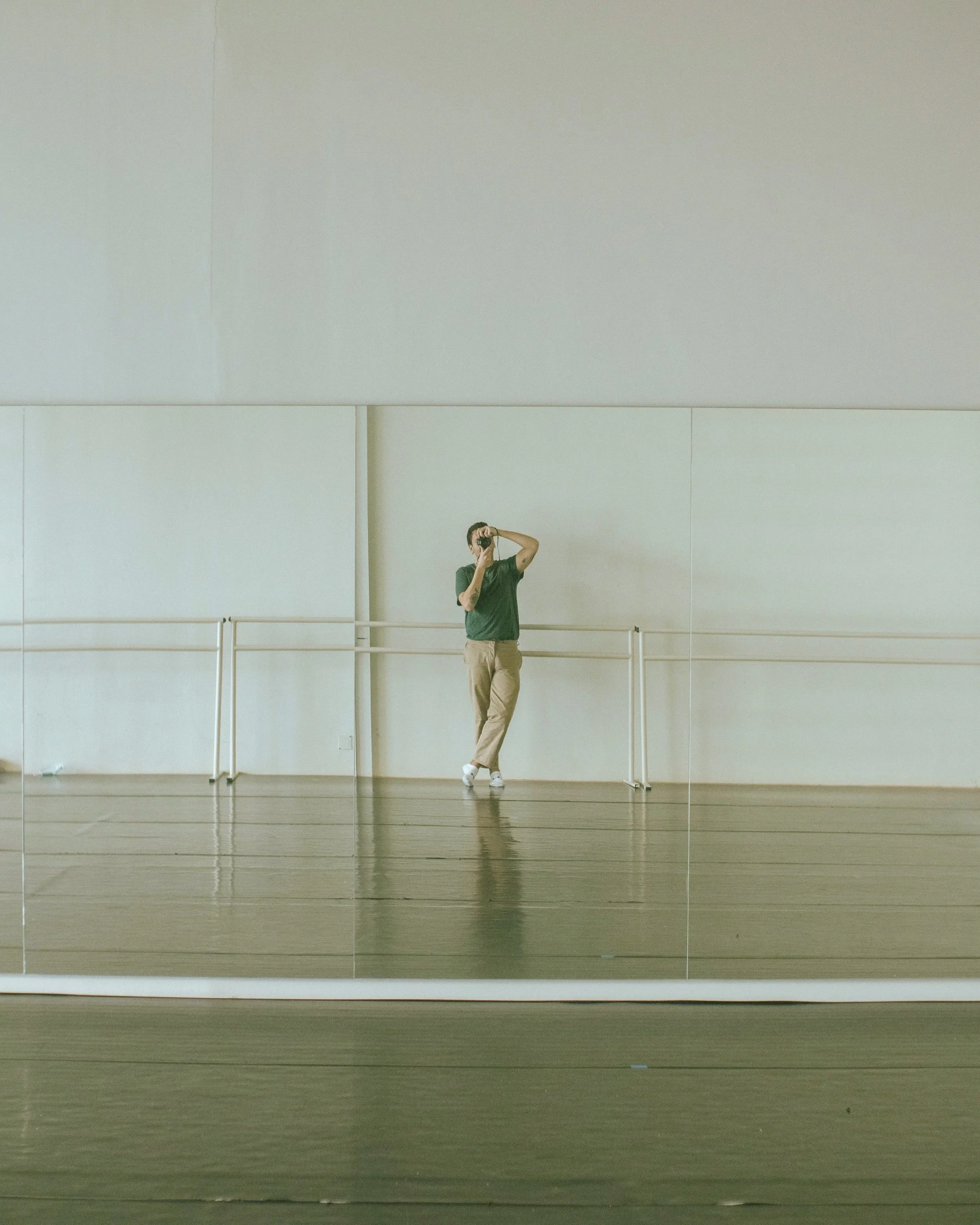 A person taking a photo in a dance studio or gym with mirrors and a ballet barre.