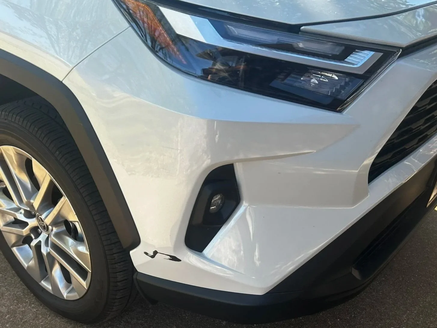 Close-up of the front right corner of a white modern SUV, showing the headlight, front tire with a multi-spoke alloy wheel, and fog light.