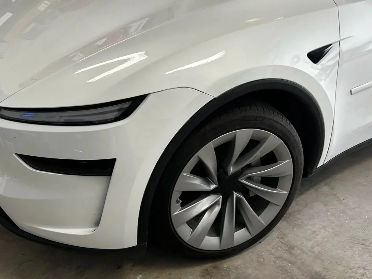 Close-up of the front part of a white electric car, showing the front wheel, sleek headlight, and modern design details.