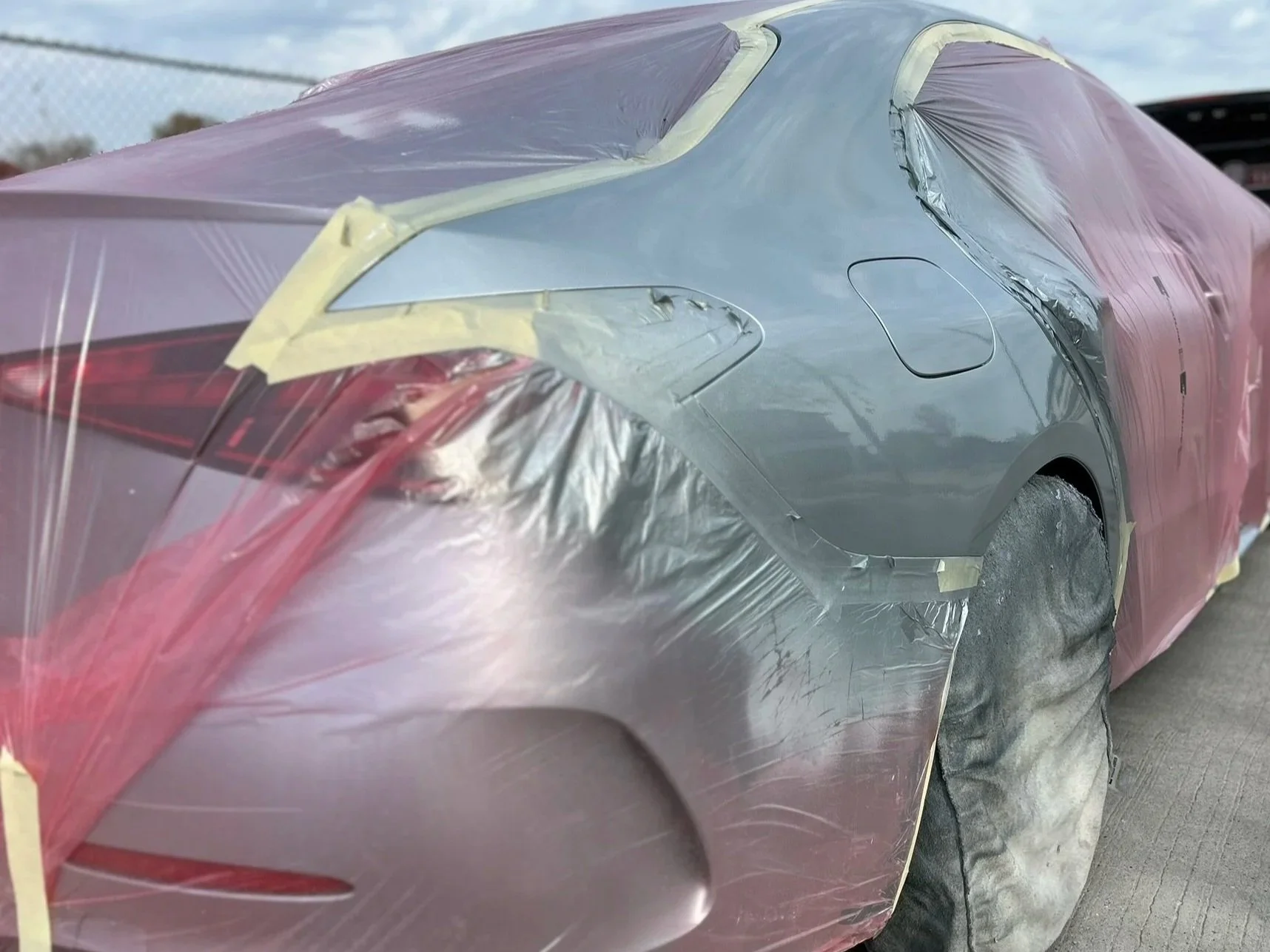 A silver car covered with masking paper and tape, likely for painting or repair work, parked outdoors.