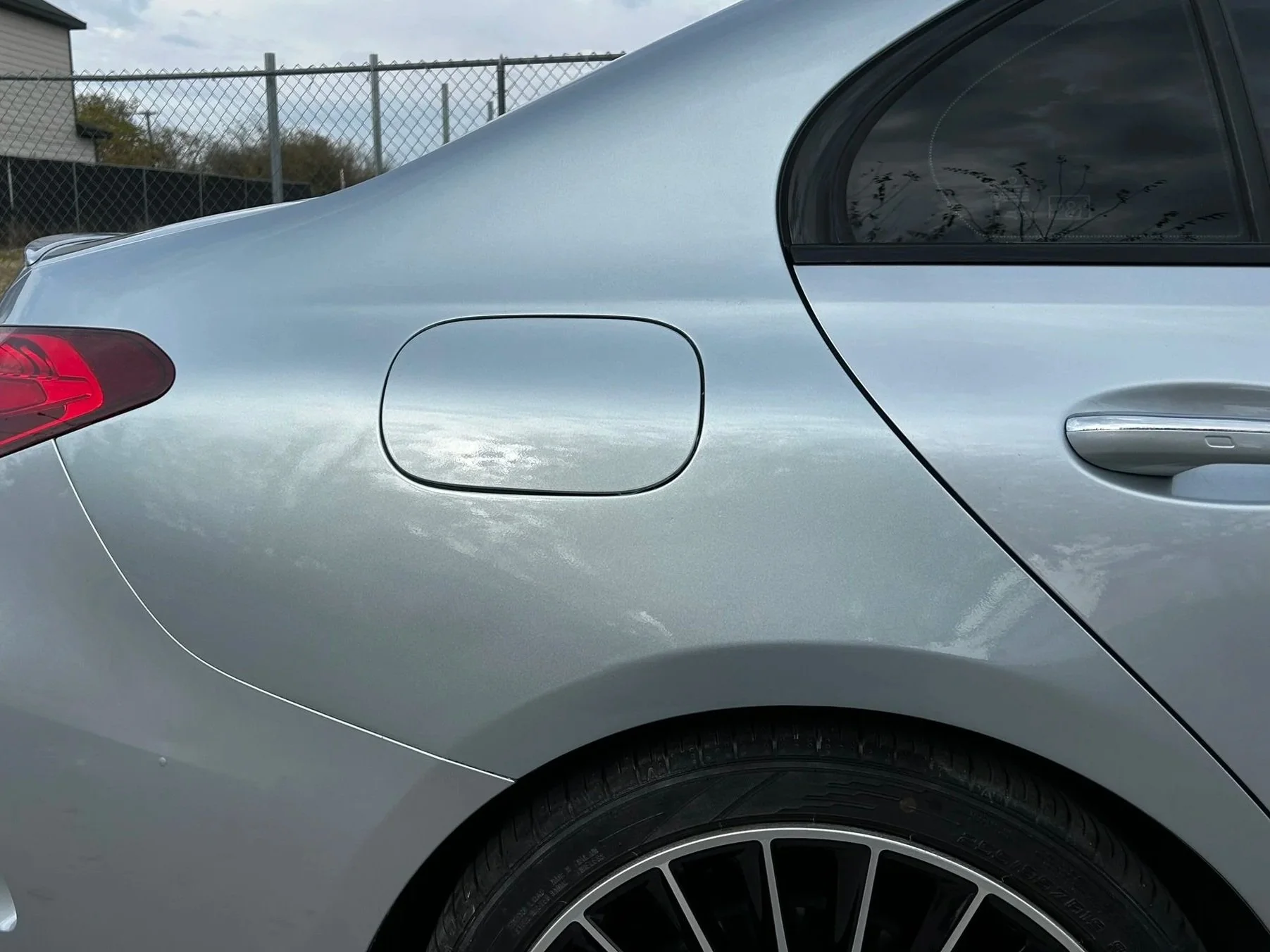 Close-up of the rear side of a silver car, showing the fuel cap, rear wheel, and a portion of the rear window.