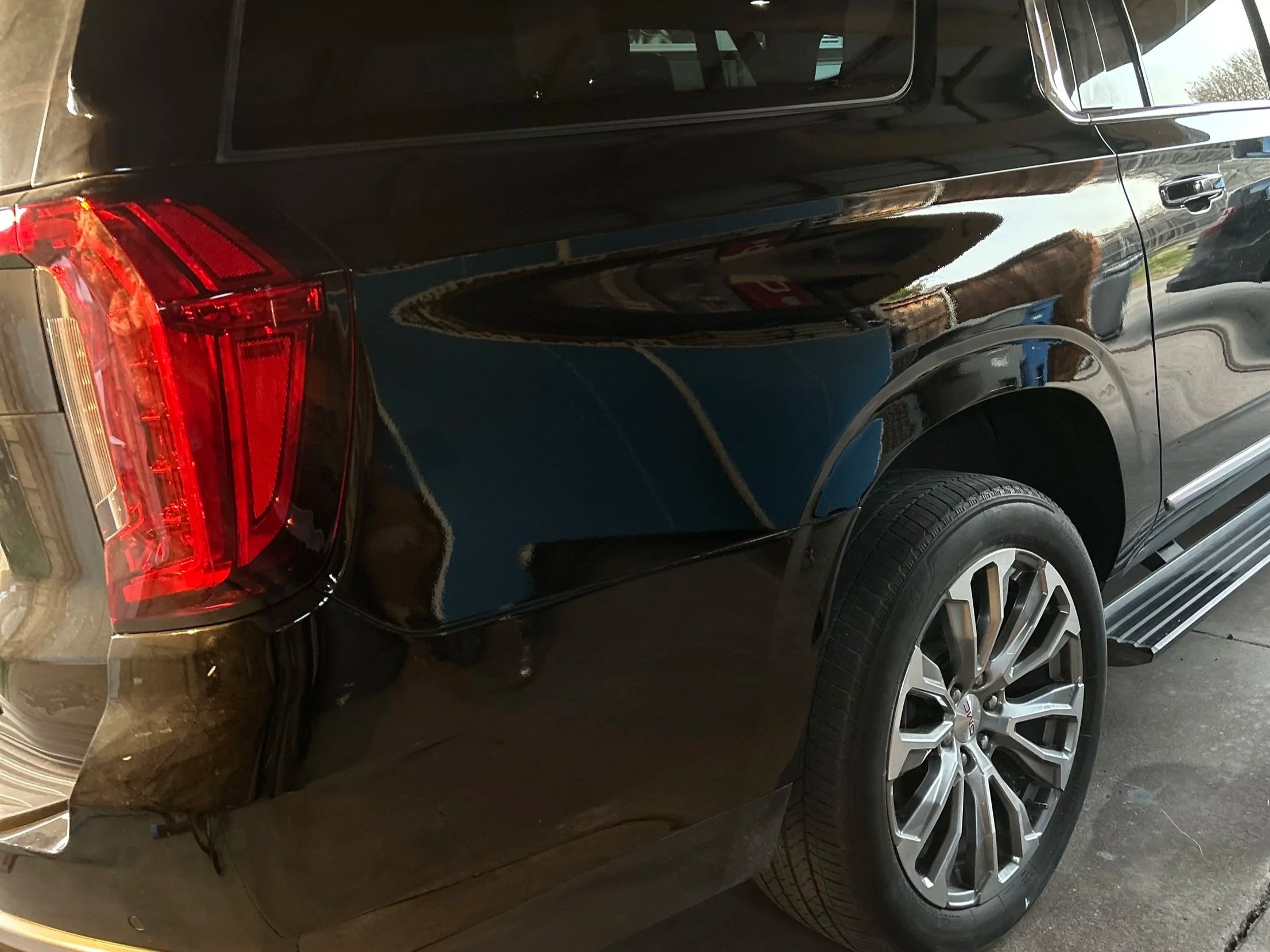 A black SUV parked in a garage, showing the rear and partial side view with red taillights and silver alloy wheels.
