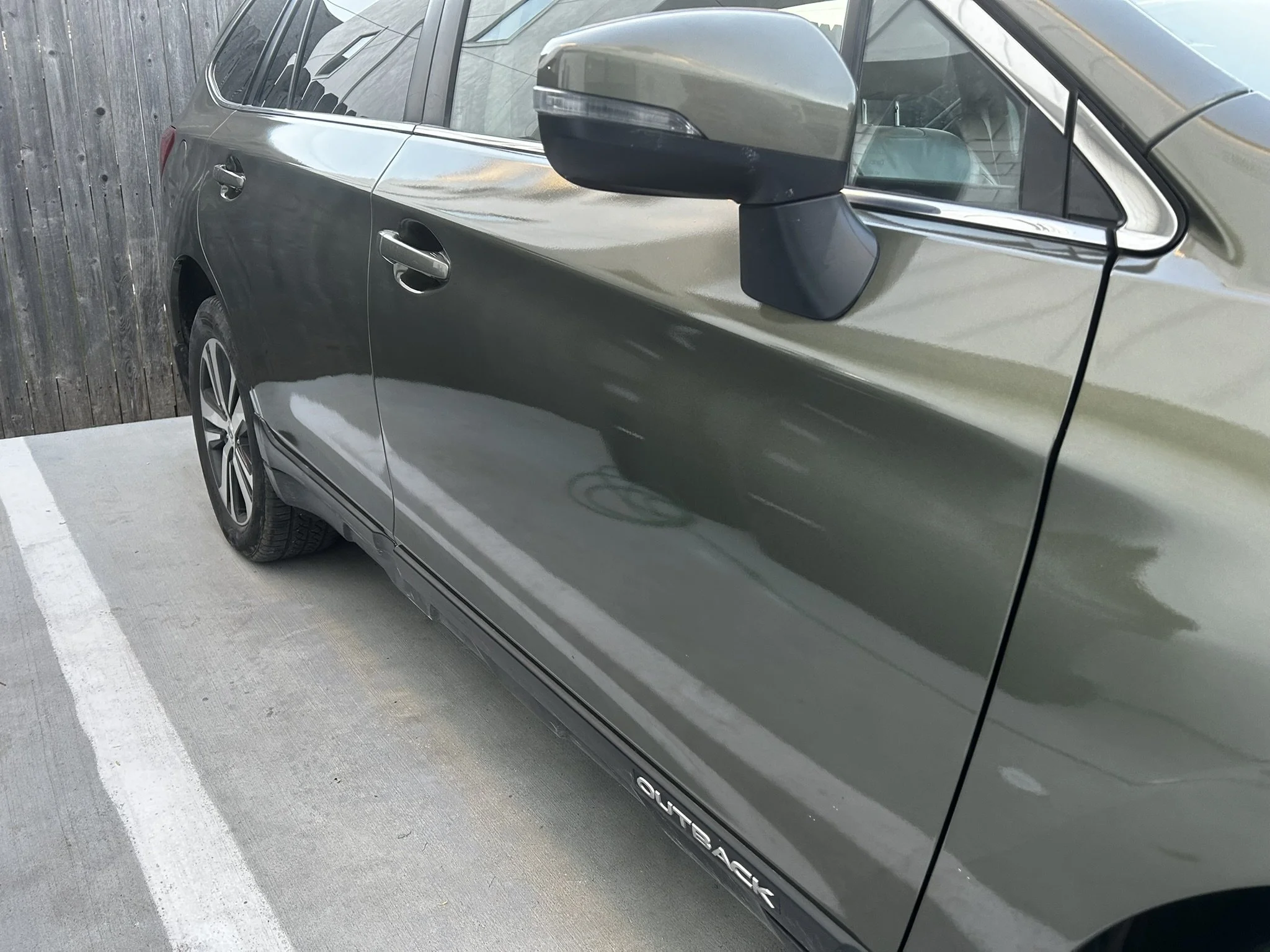 Green Subaru Outback parked in a parking space next to a wooden fence.