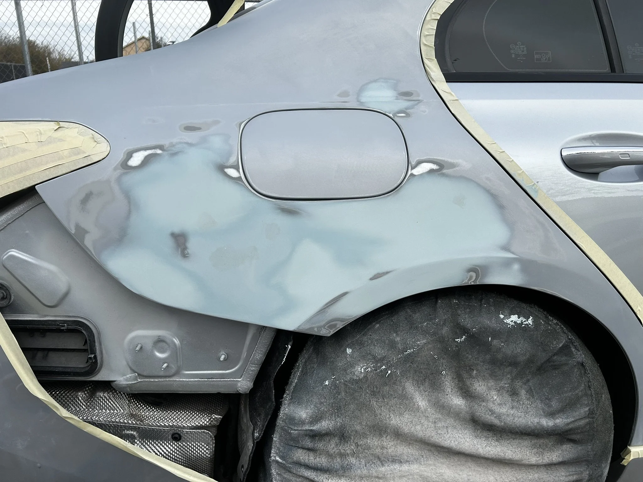 Close-up of a car being repaired, with part of the body panel removed, exposing the inner structure and a coated surface on the wheel area.