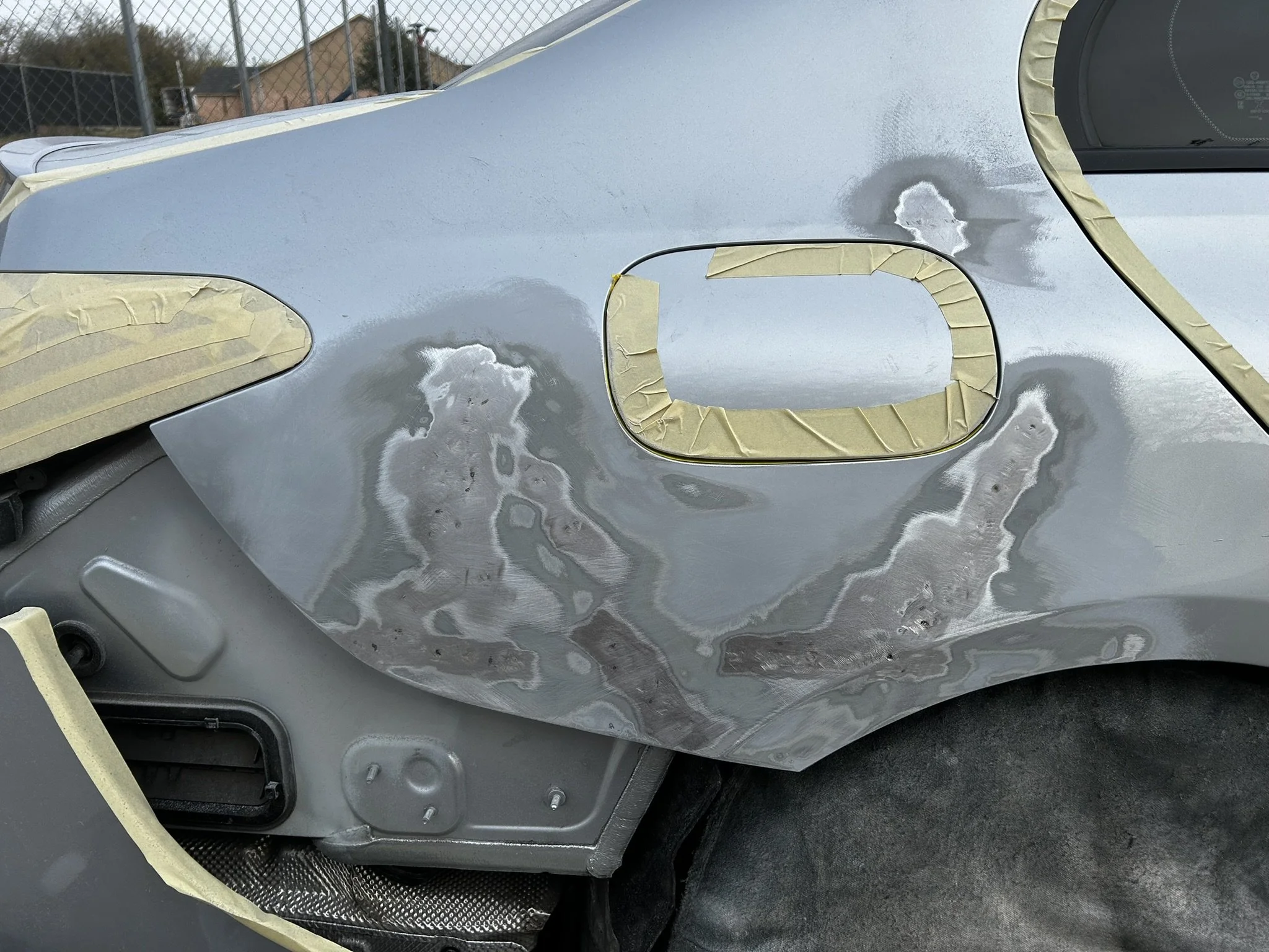 Close-up of a car in the process of repair or painting, with masked areas and sanded spots on the body.
