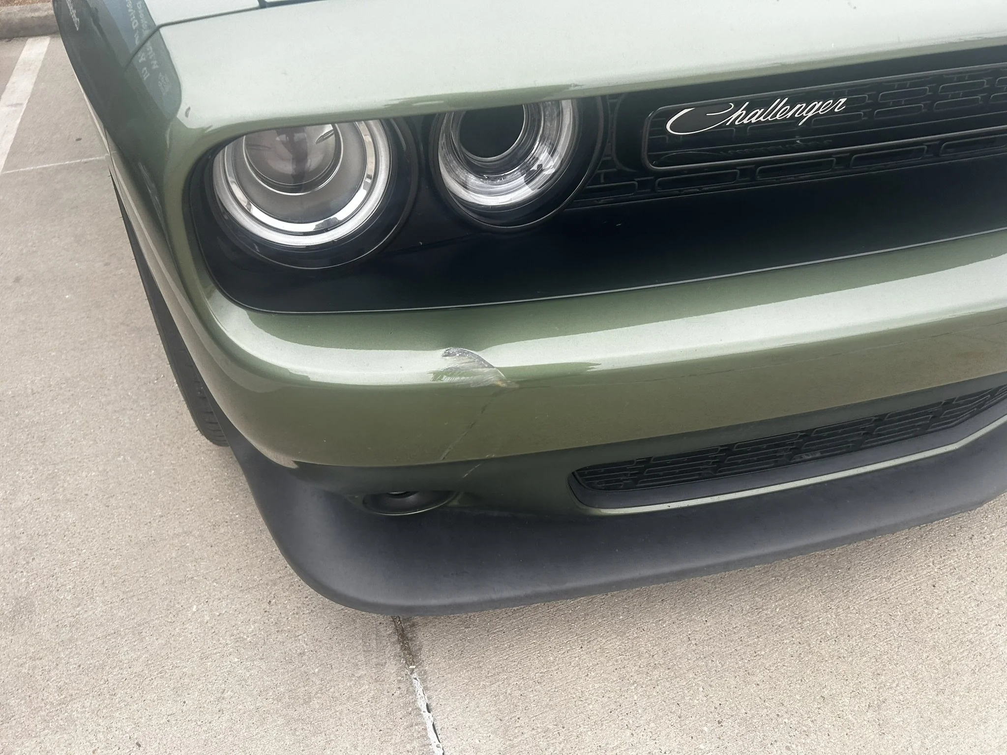 Front left of a green Dodge Challenger with a visible scratch on the bumper and slight damage to the lower front fender.
