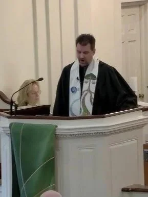 A man dressed in a black clergy robe standing inside a church.