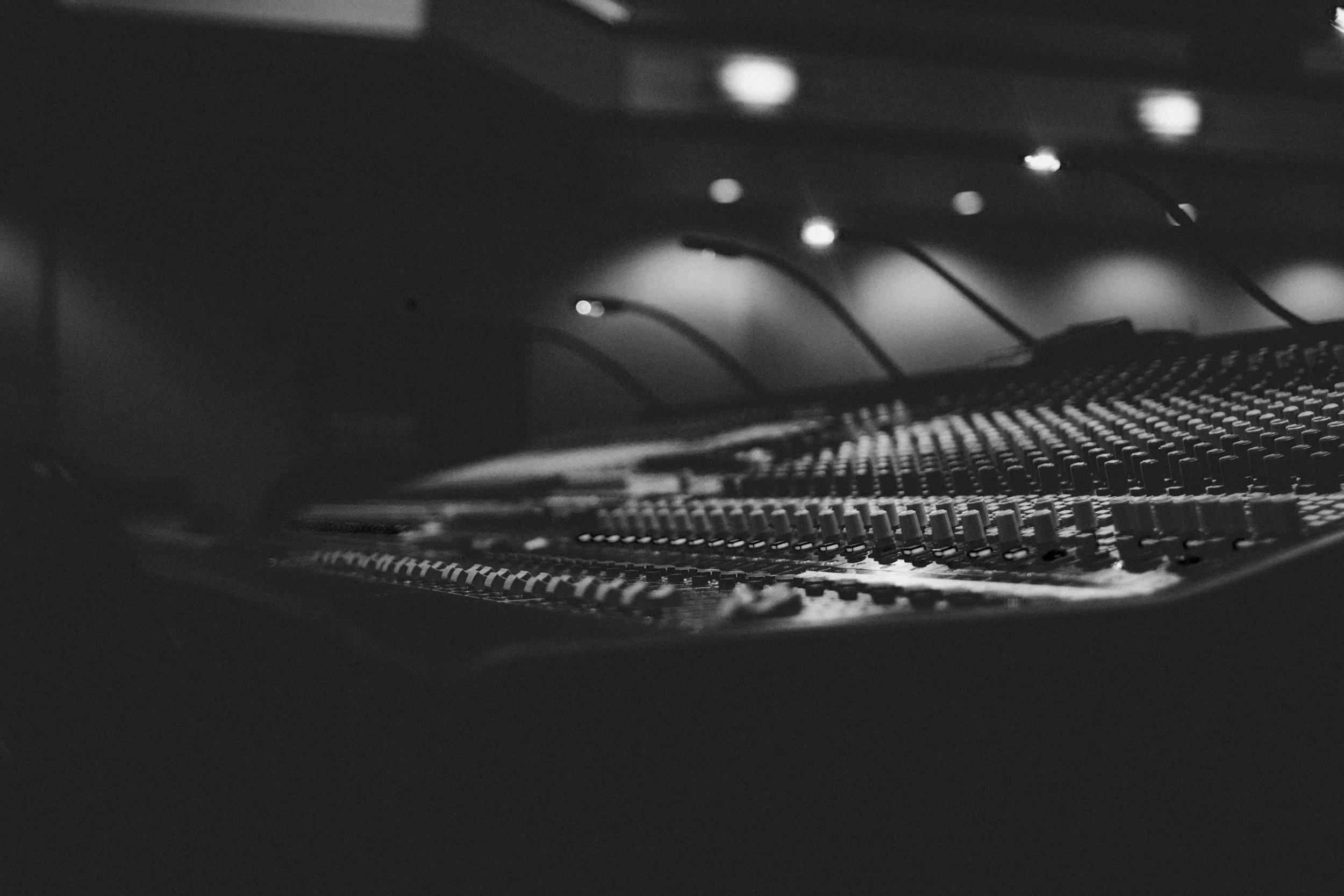 Close-up black and white photo of an audio mixing console with faders and controls.